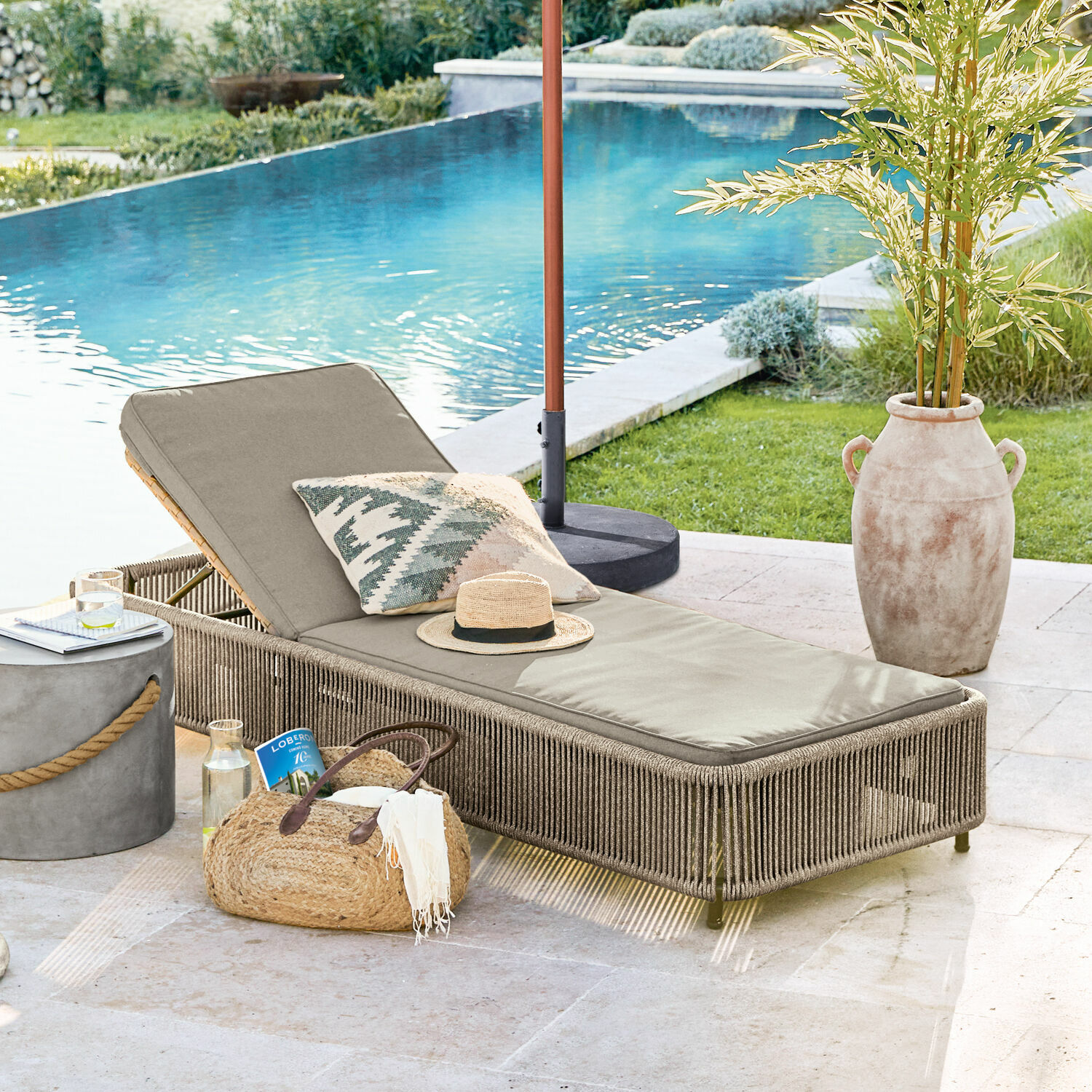 Lettino Huntville Lettino da giardino beige con cuscino e struttura intrecciata vicino alla piscina, arredo esterno