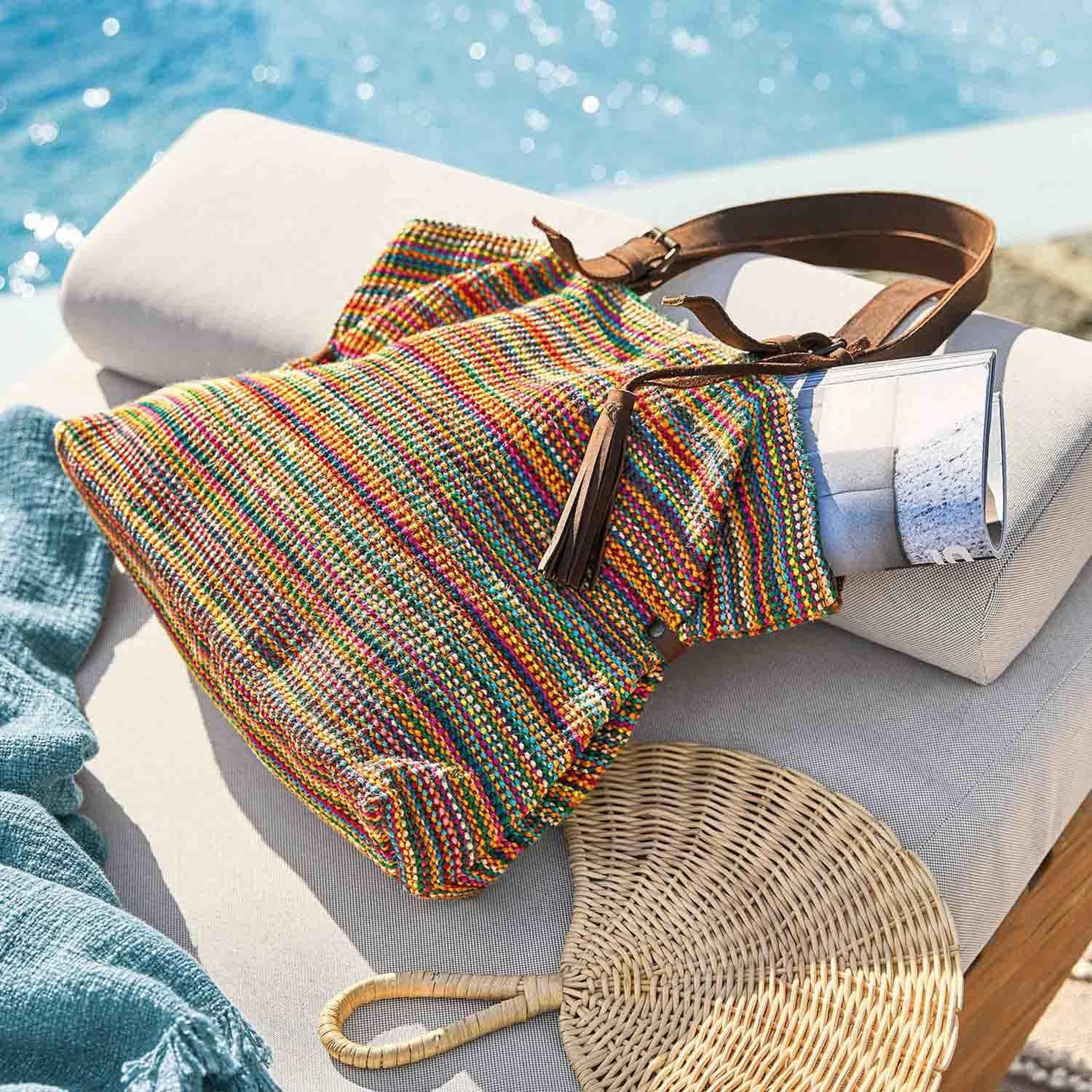 Borsa intrecciata multicolore con tracolla in pelle marrone su cuscino chiaro vicino alla piscina