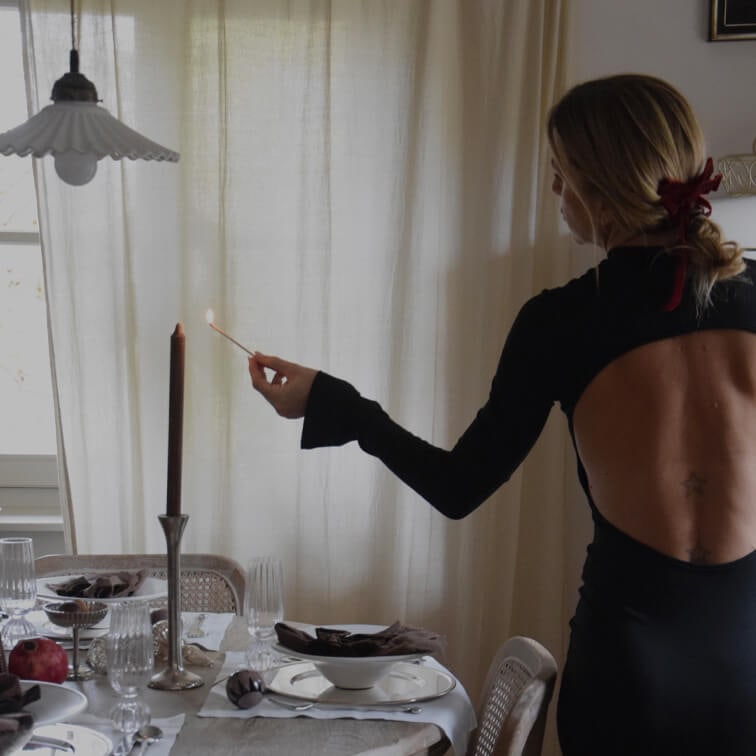 Donna in abito nero con schiena scoperta accende una candela su una tavola elegantemente apparecchiata