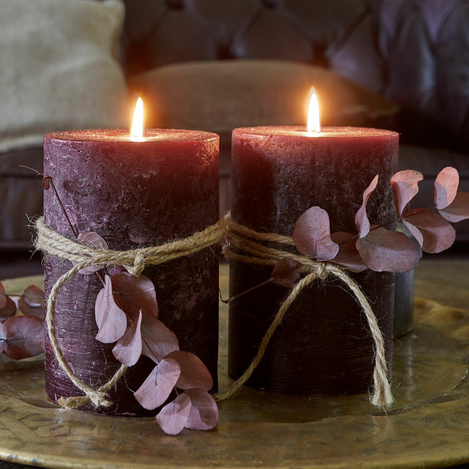 Coppia di candele Oviedo Due candele bordeaux con corda naturale e foglie secche su un vassoio decorativo in ottone