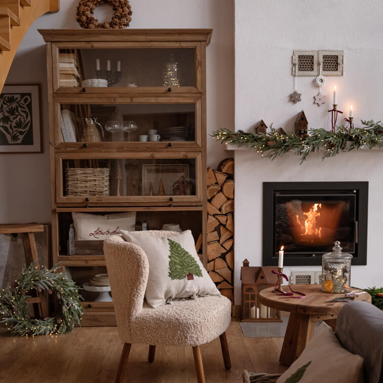 Soggiorno accogliente con poltrona crema, mobile in legno e camino decorato per Natale