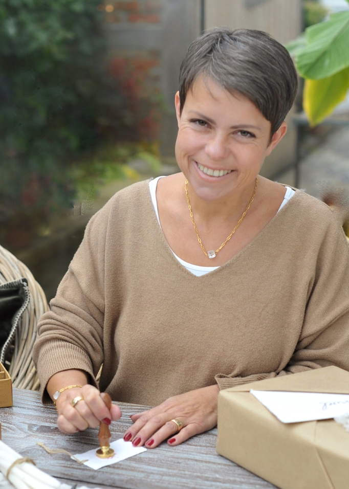 Donna con maglione beige sigilla una busta con ceralacca su tavolo di legno con regalo