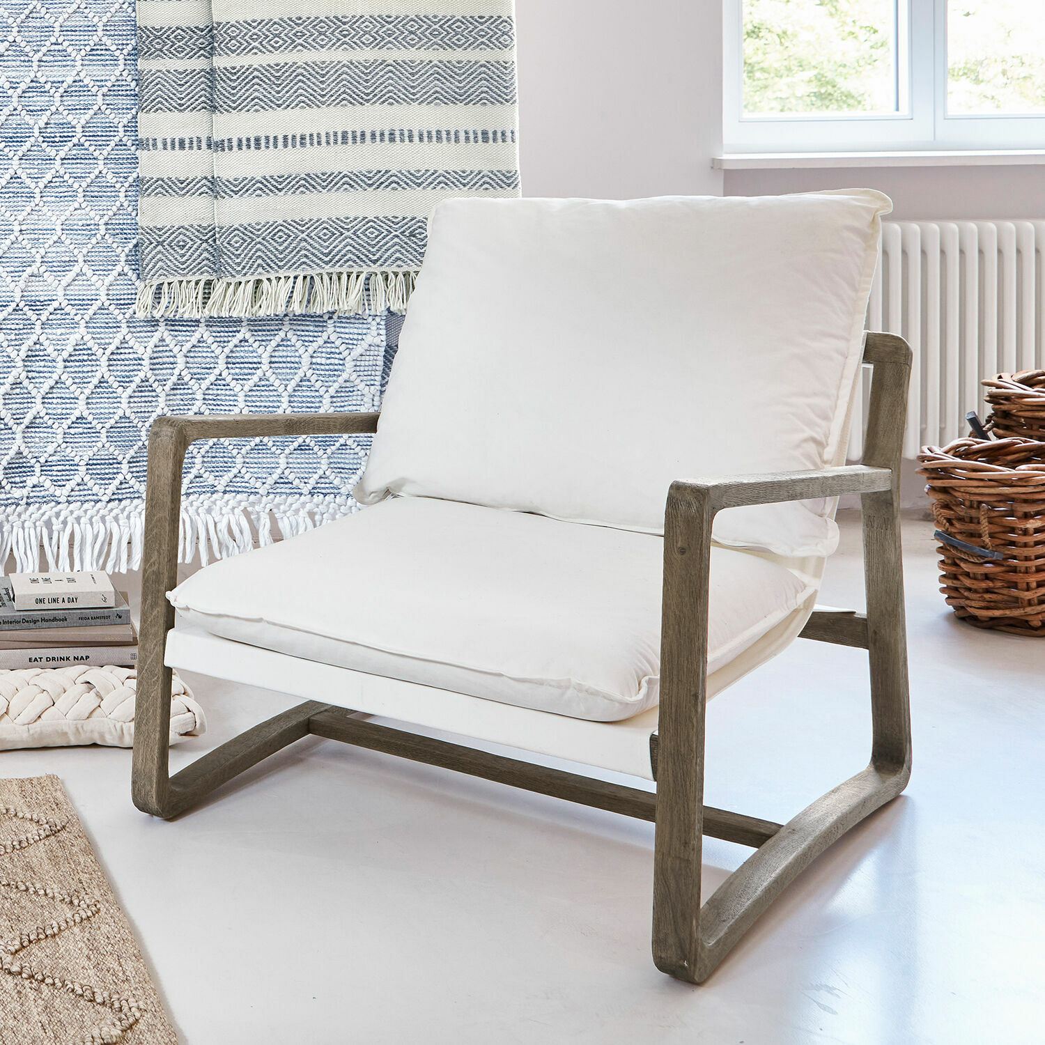 Poltrona con struttura in legno e cuscino bianco in cotone in interno luminoso e moderno