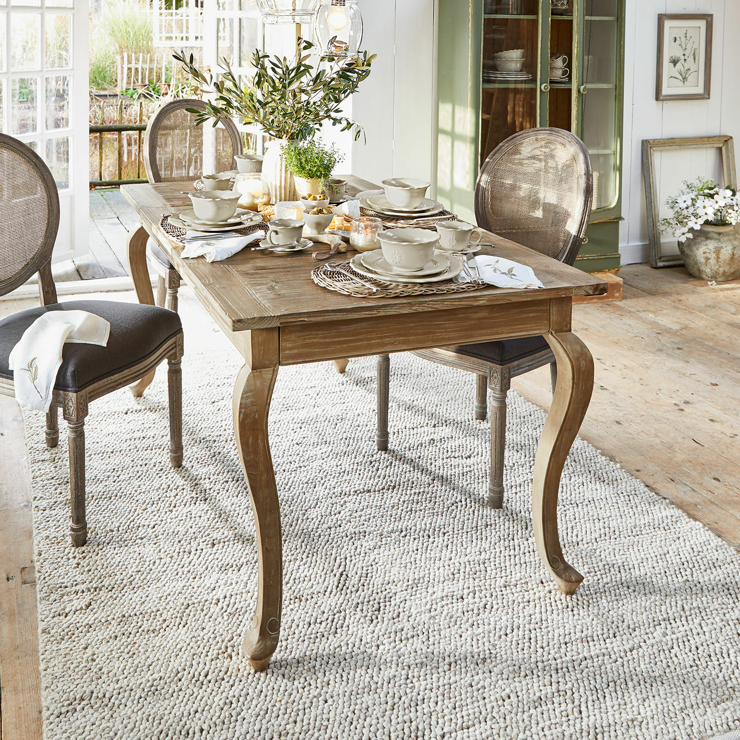 Tavolo Plaish Tavolo da pranzo rustico in legno con gambe sagomate e stoviglie chiare in ambiente luminoso