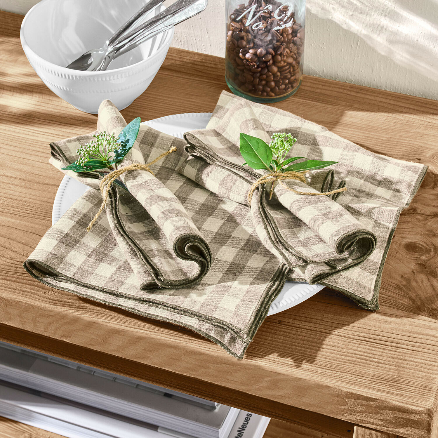 Tovaglioli di lino beige a quadri marroni con rami verdi decorativi su tavolo in legno