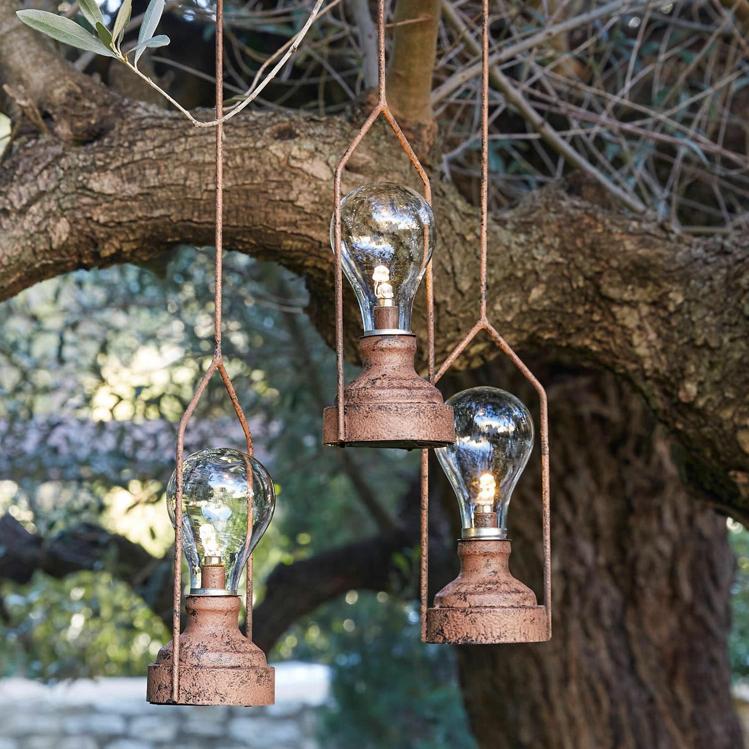 Tre lampade sospese in metallo arrugginito con lampadine LED davanti a un albero, illuminazione decorativa da giardino
