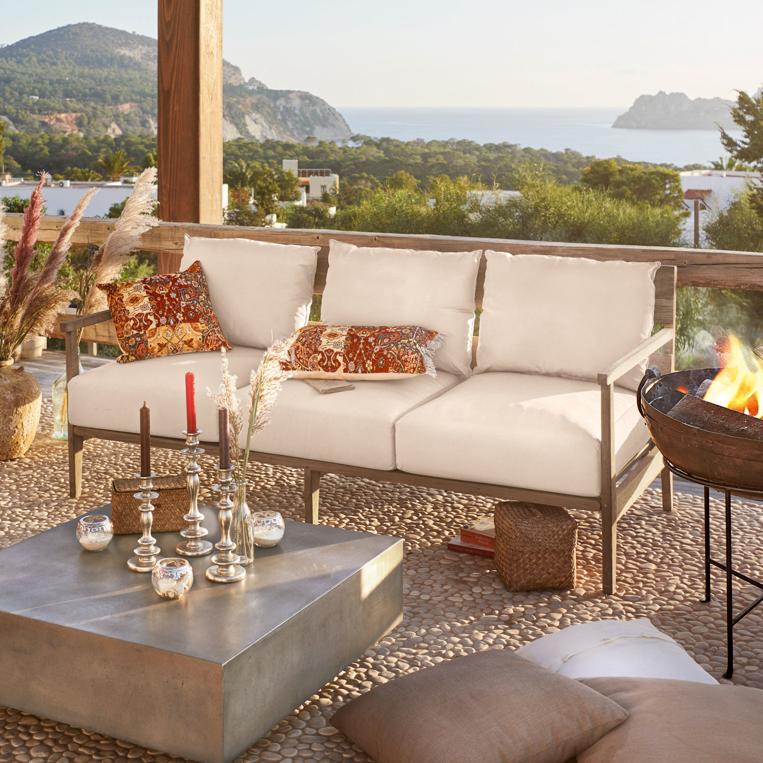 Divano Kingsbridge Divano da esterno beige con struttura in legno e cuscini colorati su terrazza con vista mare