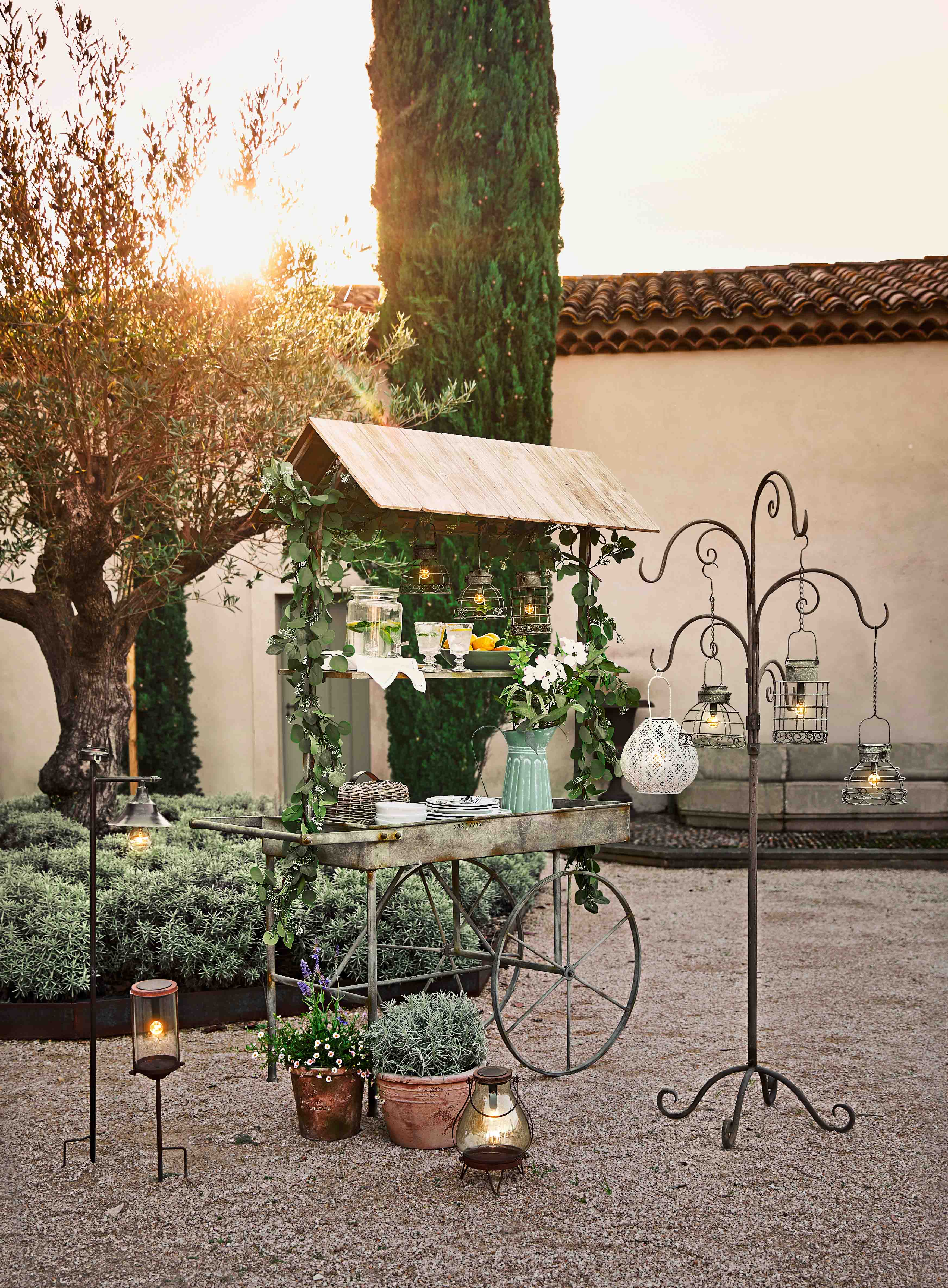 Carrello da giardino in metallo con tetto in legno, decorazioni vegetali e lanterne appese all'aperto