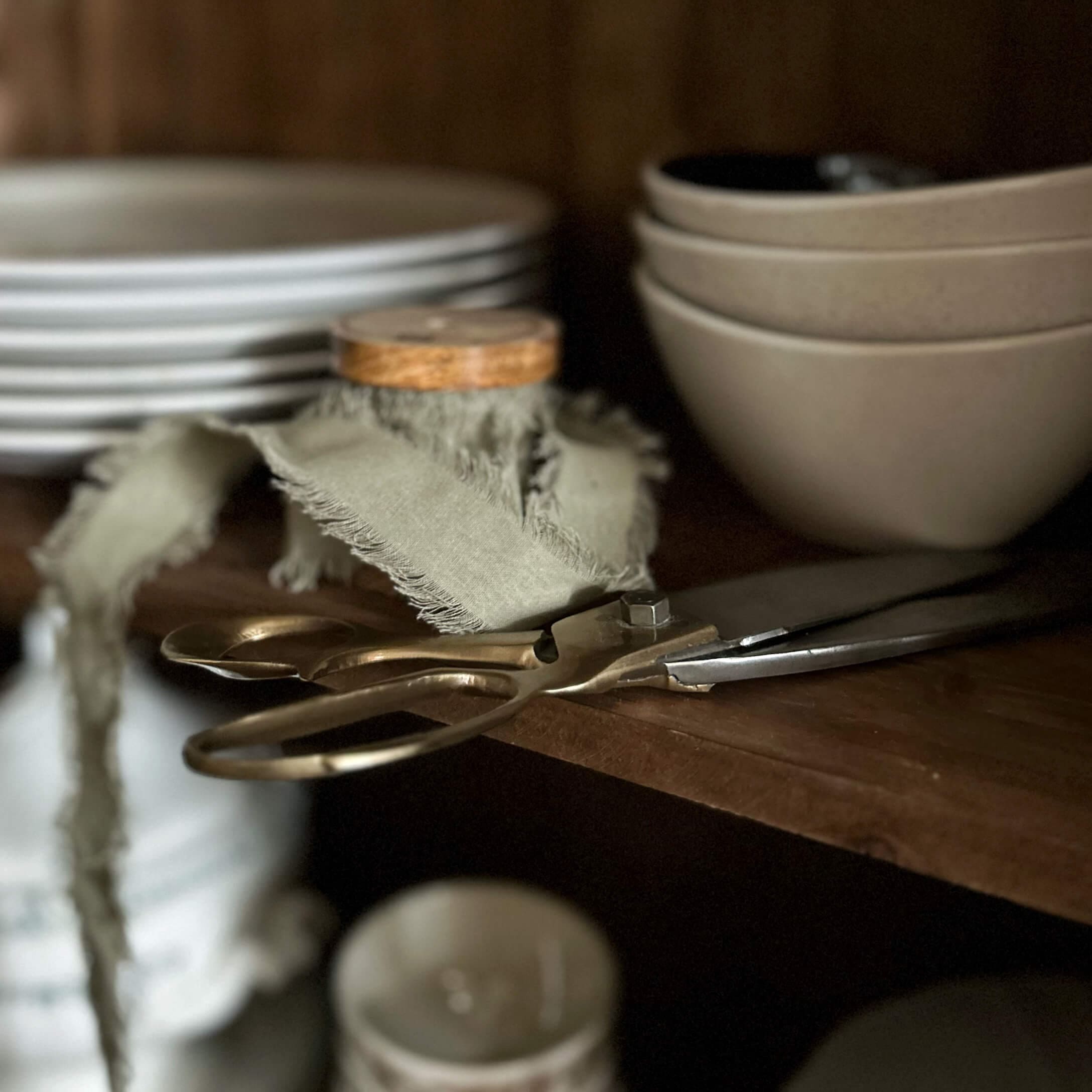 Vecchie forbici in ottone su mensola di legno accanto a ciotole e piatti beige in cucina
