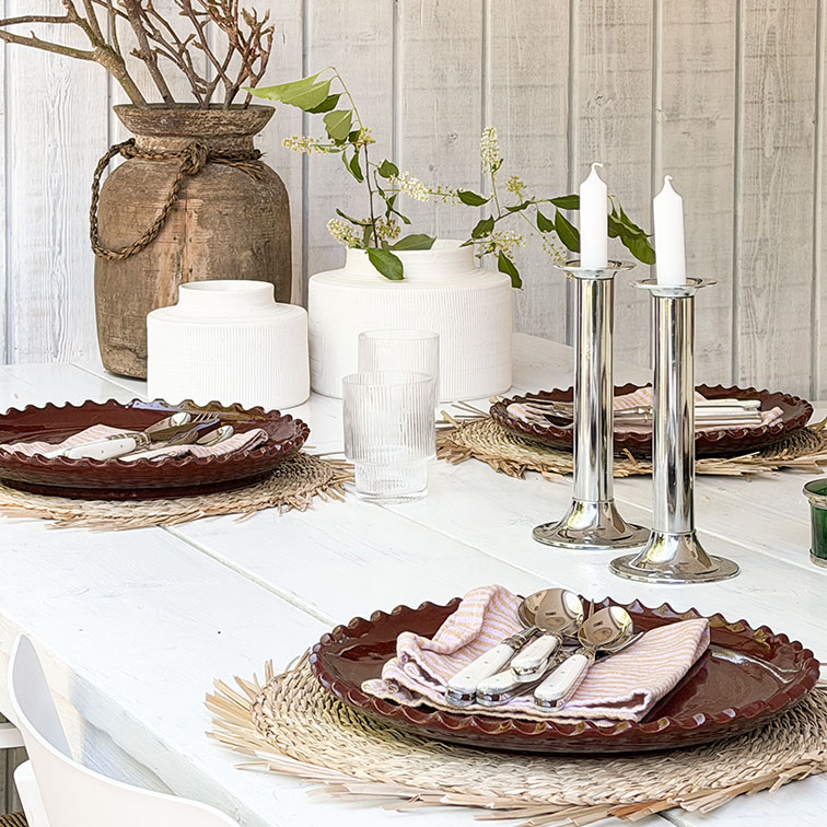 Tavolo in legno bianco con piatti in ceramica marrone e candelabri argentati su tovagliette decorative