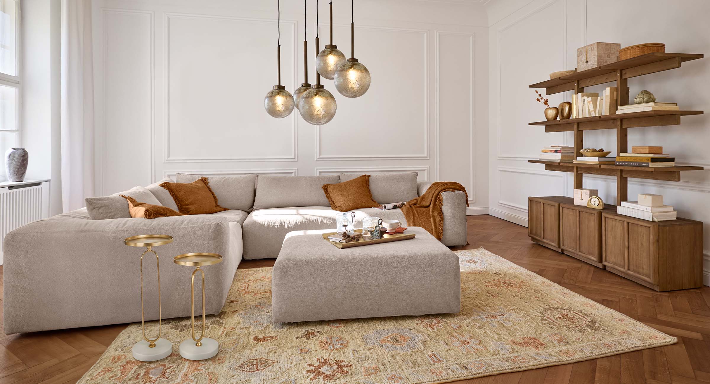 Soggiorno accogliente con divano beige, cuscini marroni e scaffale in legno in tonalità naturali