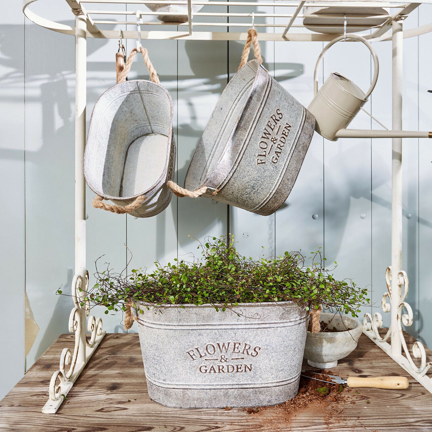 Set di 3 portavasi Merrin Vasi in metallo grigio con scritta Flowers & Garden, pianta verde e attrezzo da giardino su tavolo in legno
