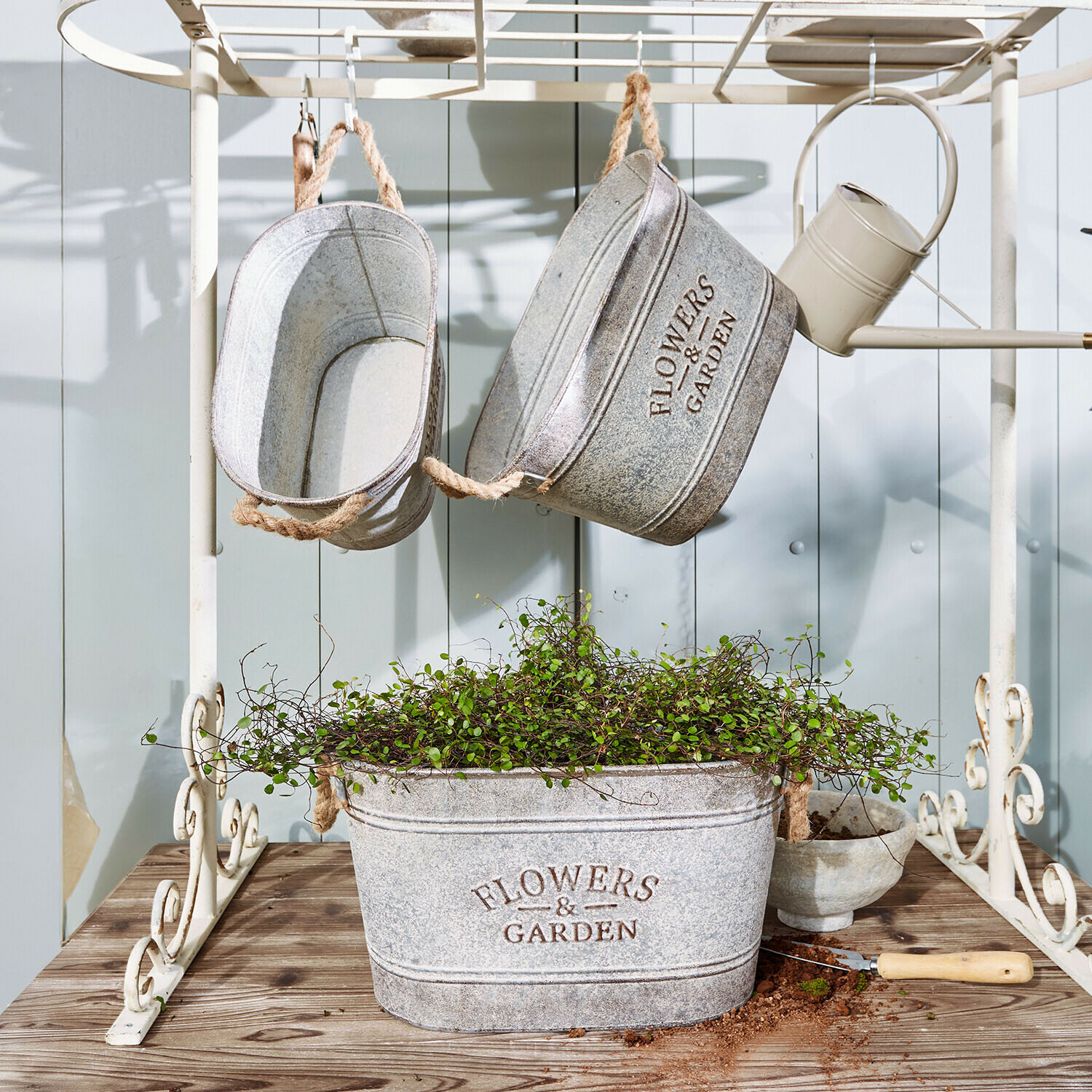 Set di 3 portavasi Merrin Vasi in metallo grigio con scritta Flowers & Garden, pianta verde e attrezzo da giardino su tavolo in legno