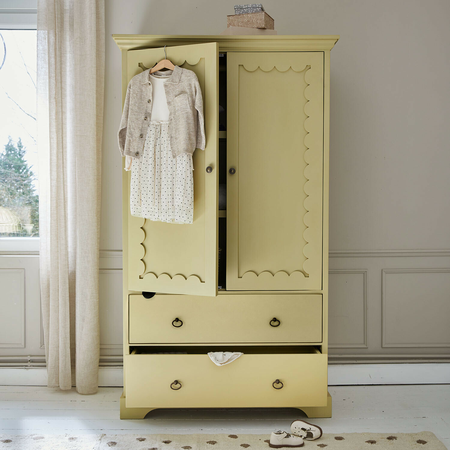 Armadio per bambini Frollin Armadio in legno giallo con ante decorative e abbigliamento per bambini appeso in una stanza luminosa