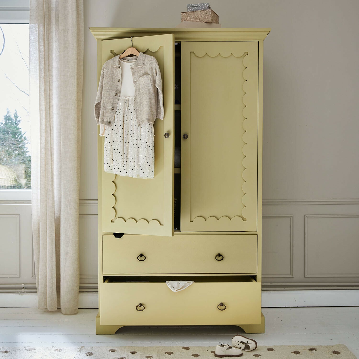 Armadio per bambini Frollin Armadio in legno giallo con ante decorative e abbigliamento per bambini appeso in una stanza luminosa
