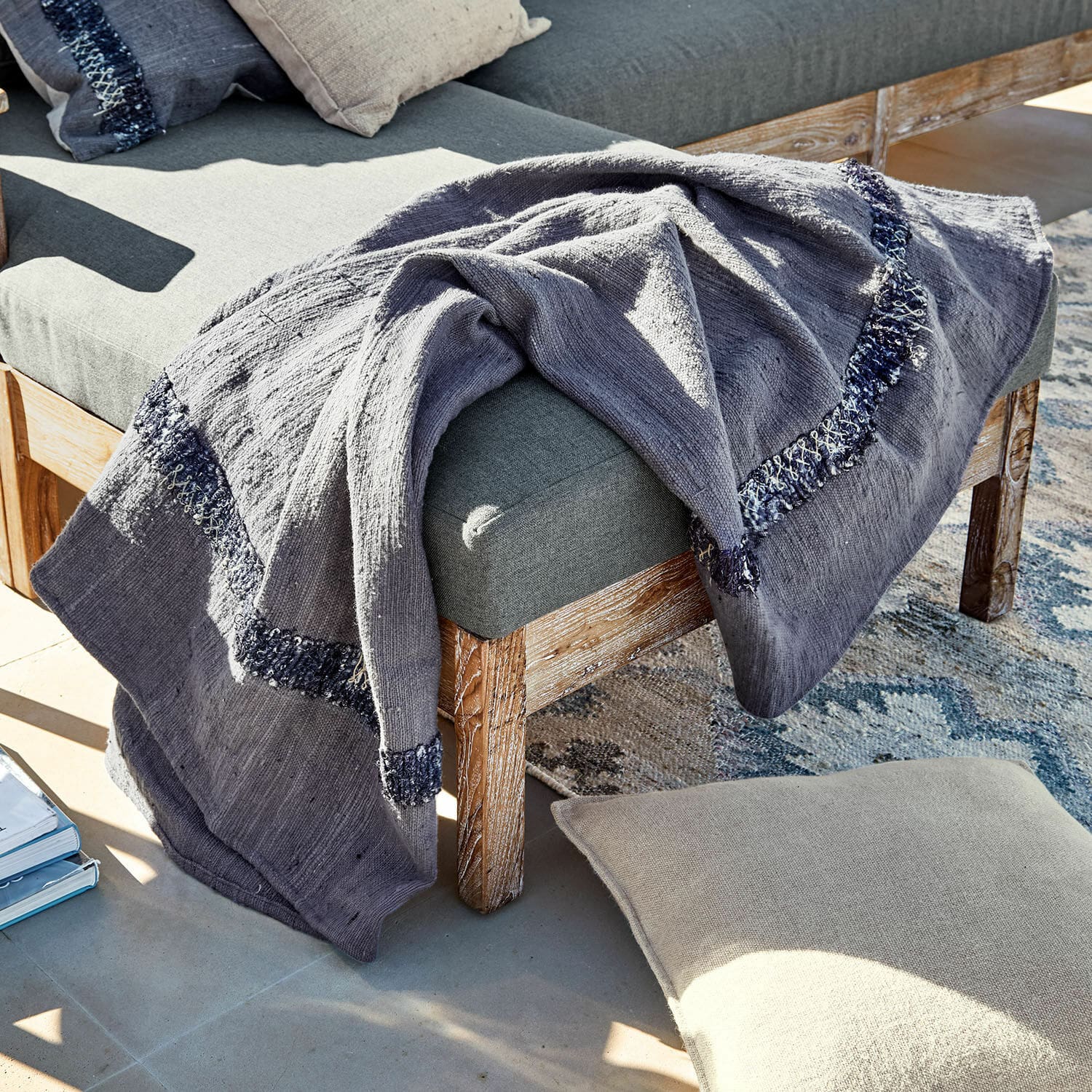 Plaid Foix Coperta grigia in cotone con motivo blu scuro su panca in legno e cuscino beige