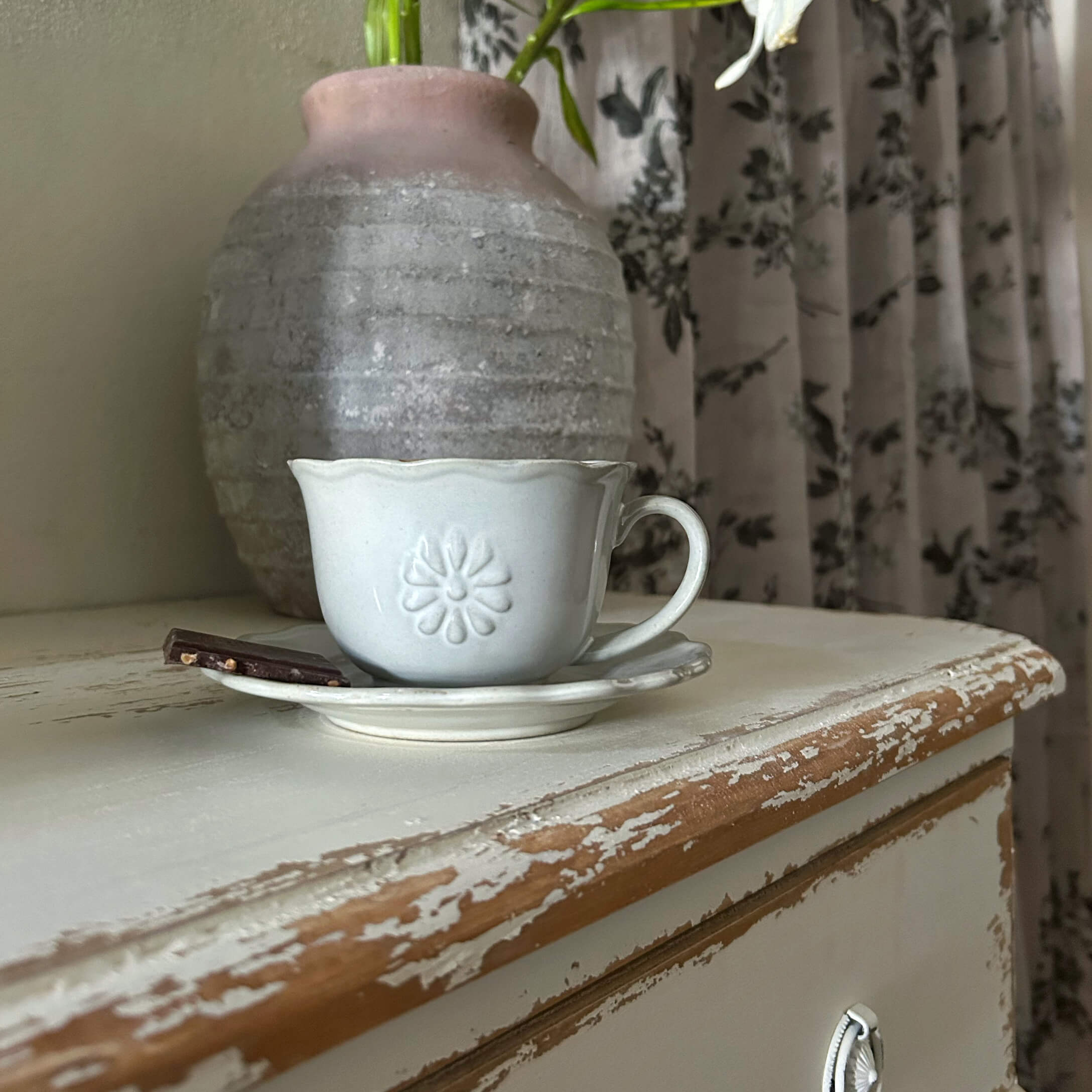 Tazza in ceramica bianca con piattino e pezzo di cioccolato su tavolo in legno invecchiato