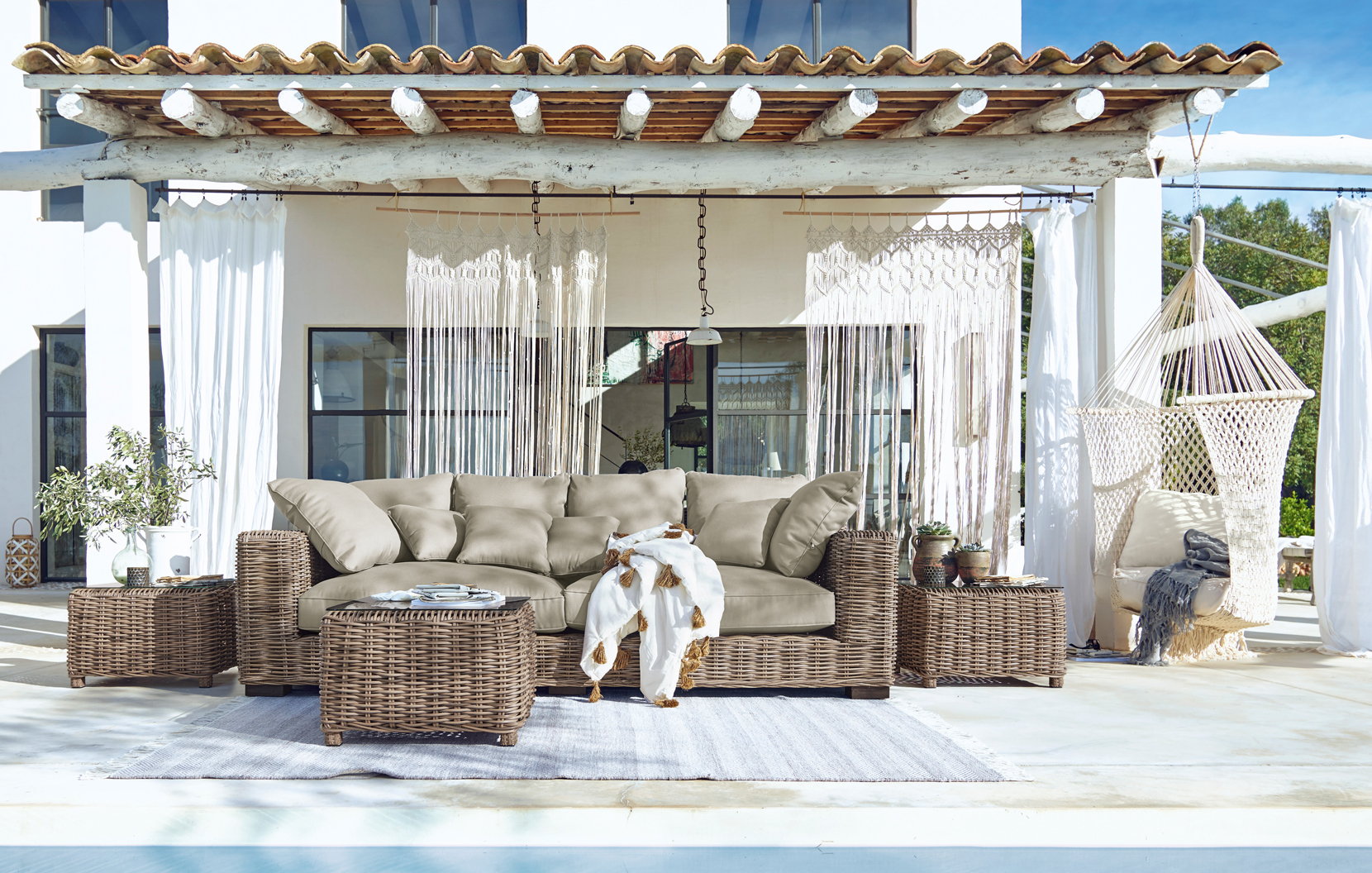 Set di mobili da giardino in rattan con cuscini beige su terrazza con amaca e decorazioni boho