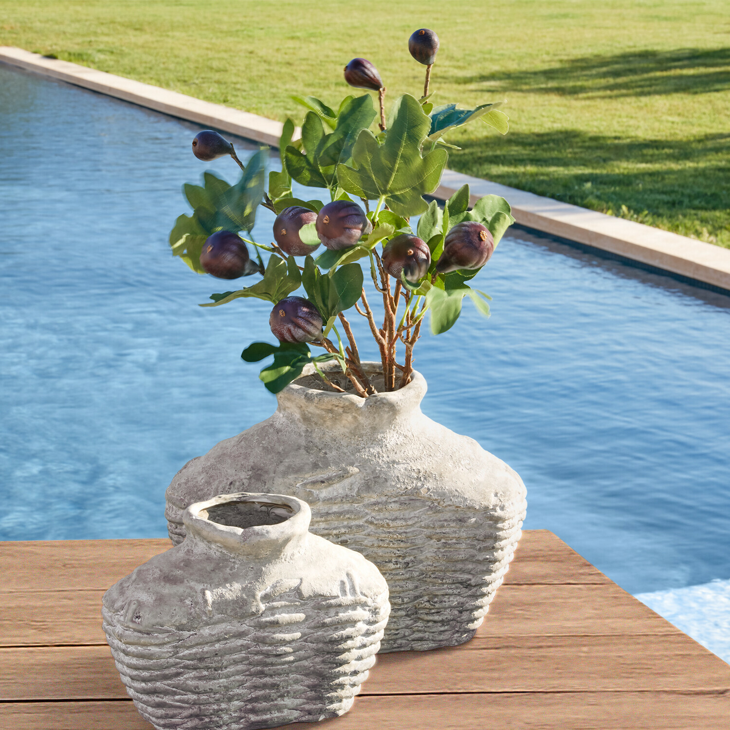 Due anfore rustiche in ceramica grigia su tavolo in legno vicino piscina con foglie verdi e frutti