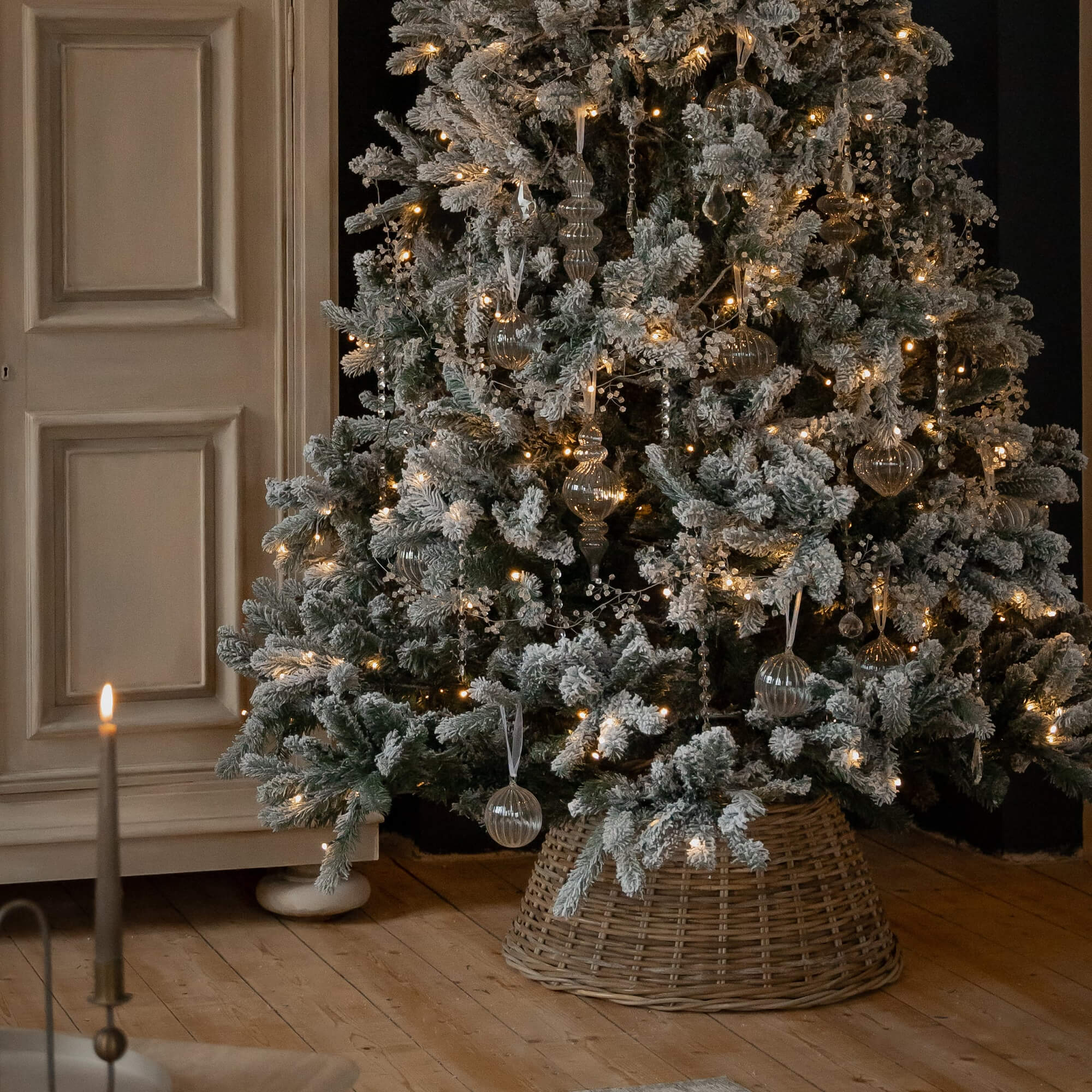 Albero di Natale innevato con decorazioni in vetro e luci calde su base in vimini