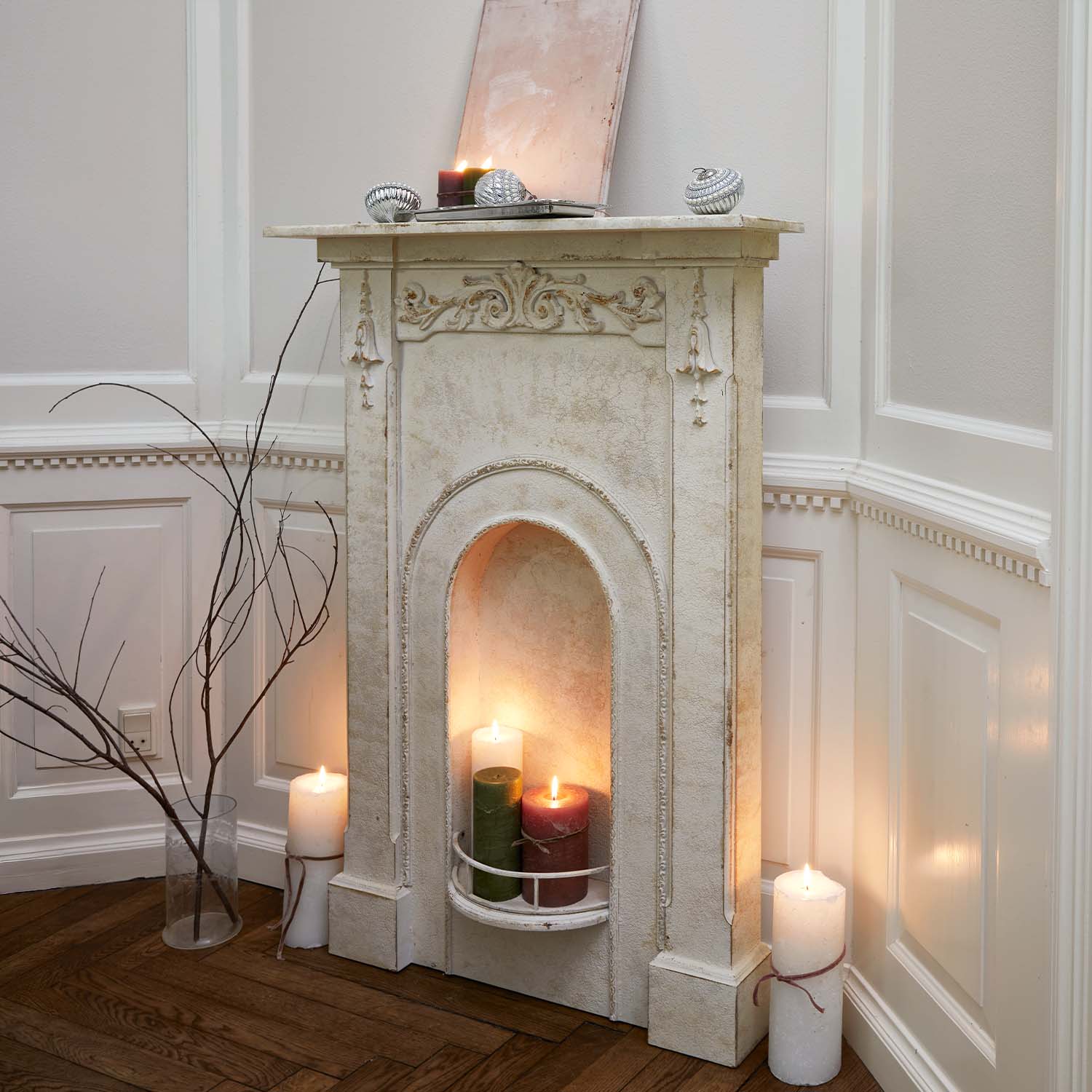 Camino decorativo bianco con rilievi ornamentali e candele accese in interno rustico