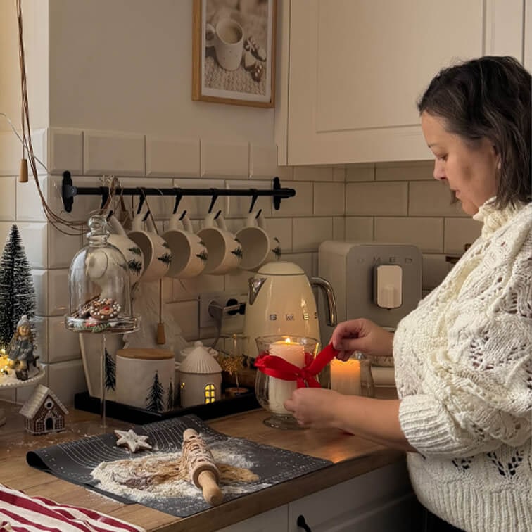 Donna con maglione bianco decora candela con nastro rosso in cucina accogliente con utensili da forno