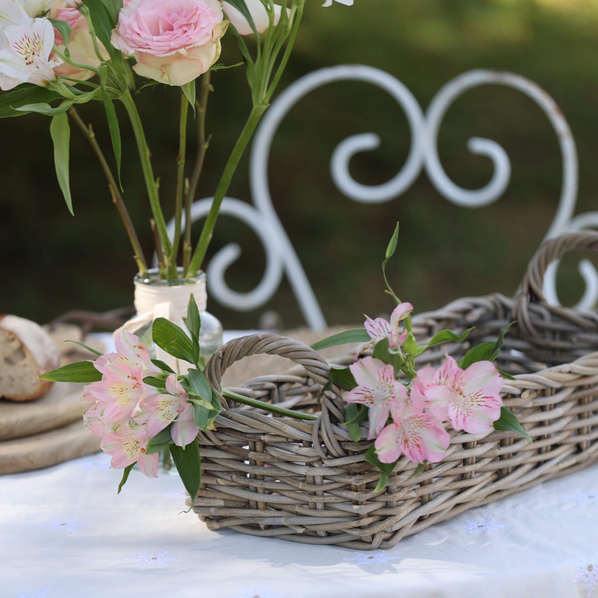 Cesto in vimini grigio con manici decorato con fiori rosa su tovaglia bianca in giardino