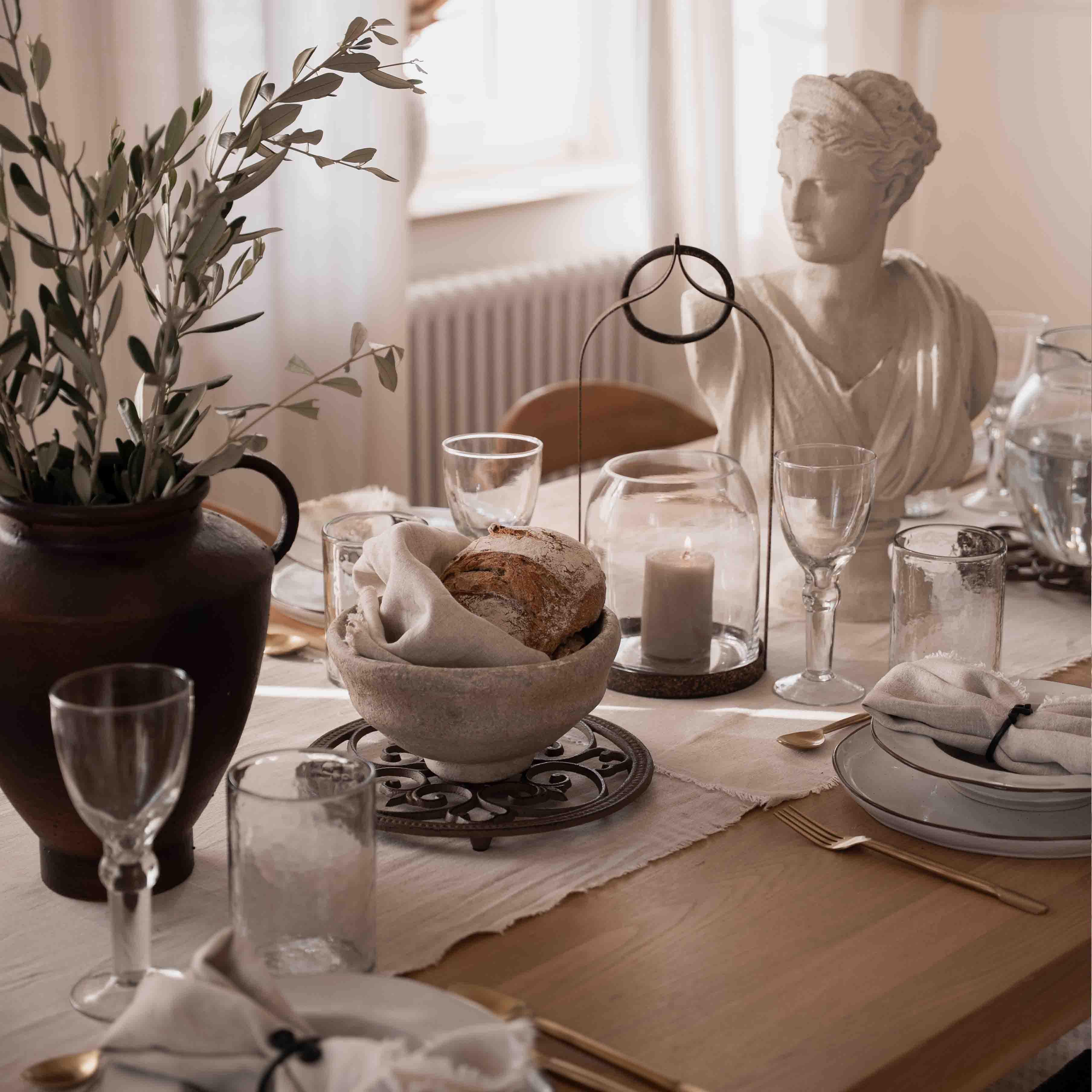 Decorazione da tavola sobria con pane, candela e statua in pietra bianca alla luce naturale