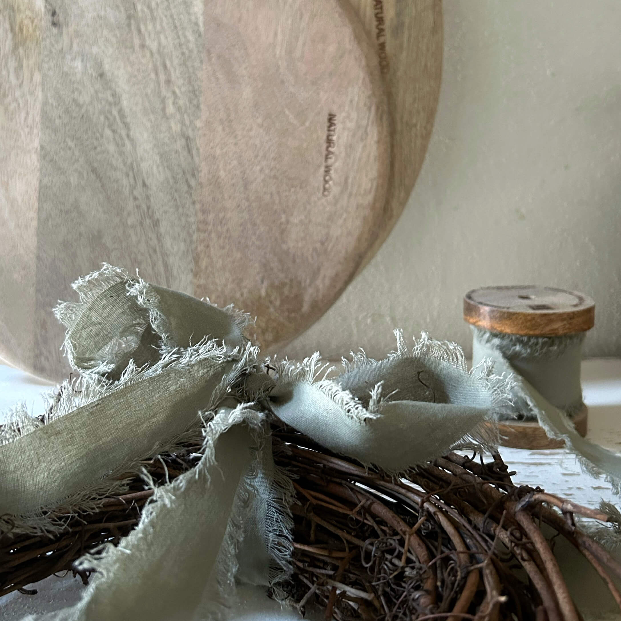 Piatto in legno naturale con nastro di lino grigio su corona di vimini per decorazione d'interni