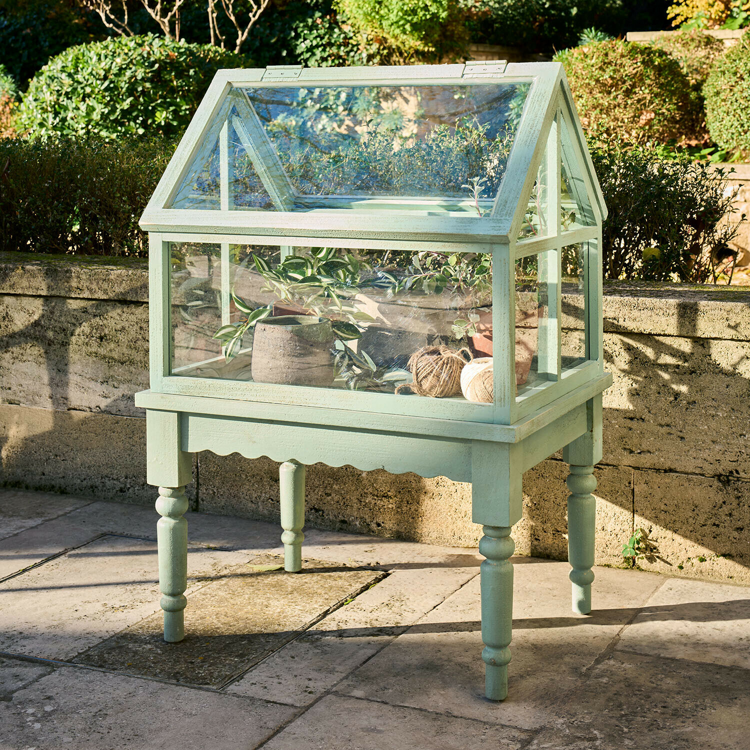 Piccola serra verde in legno su gambe con piante e rotoli di spago per il giardino