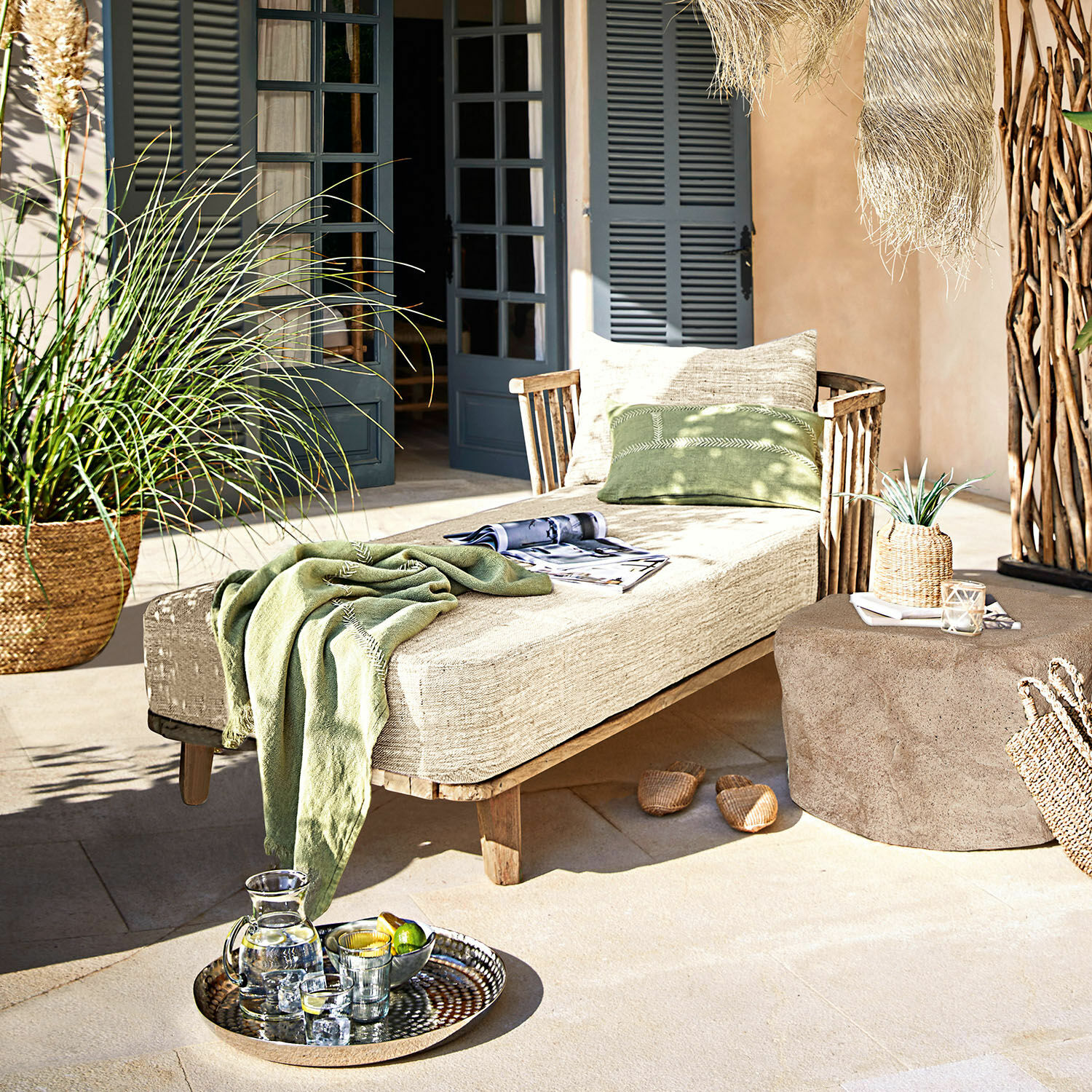 Chaise-longue Bellville Lettino in legno con cuscino beige e coperta verde su terrazza decorata con vassoio di bevande