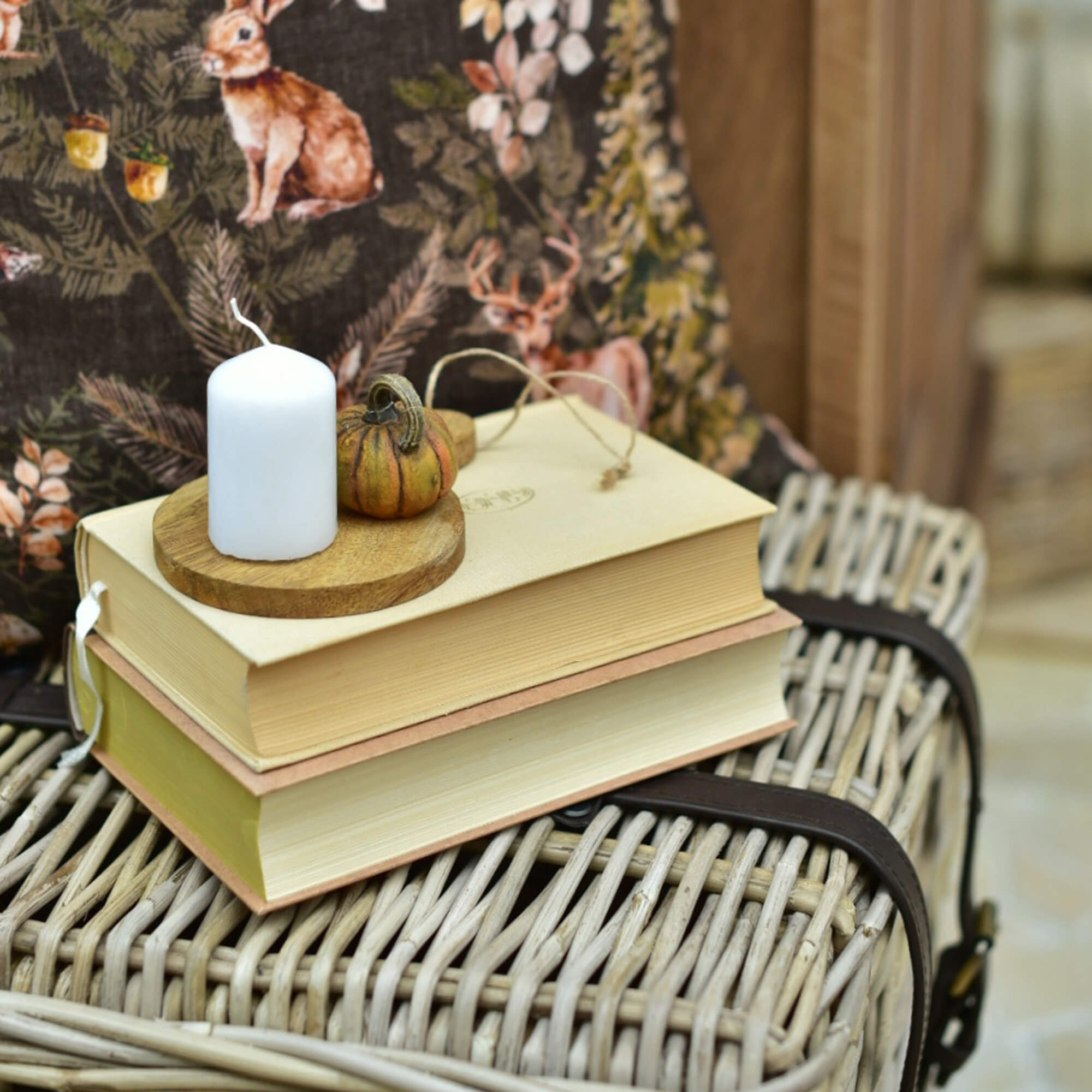 Candela bianca e piccola zucca decorativa su base in legno sopra pila di libri su valigia in vimini