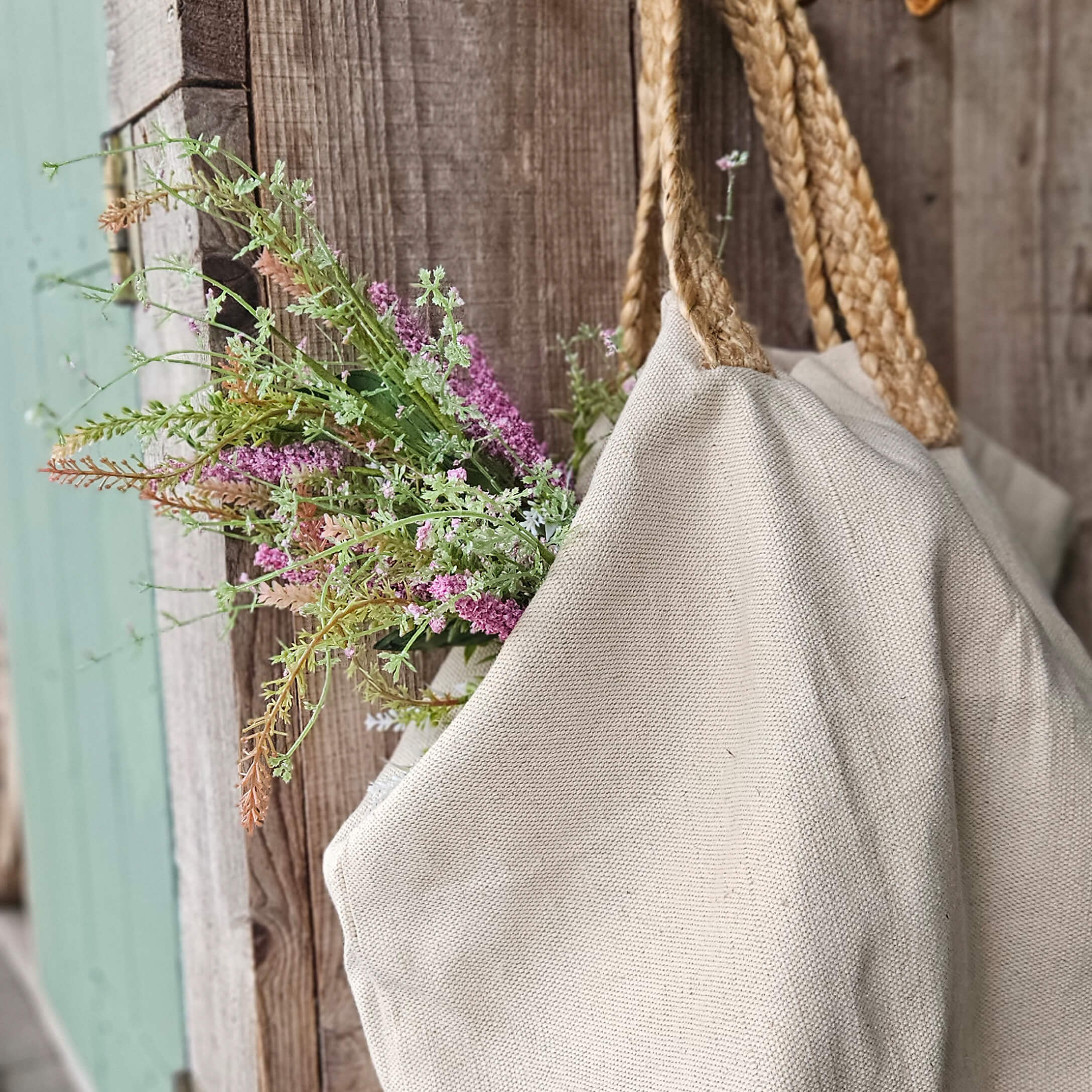 Borsa beige in materiale naturale con manici intrecciati e fiori su sfondo di legno rustico