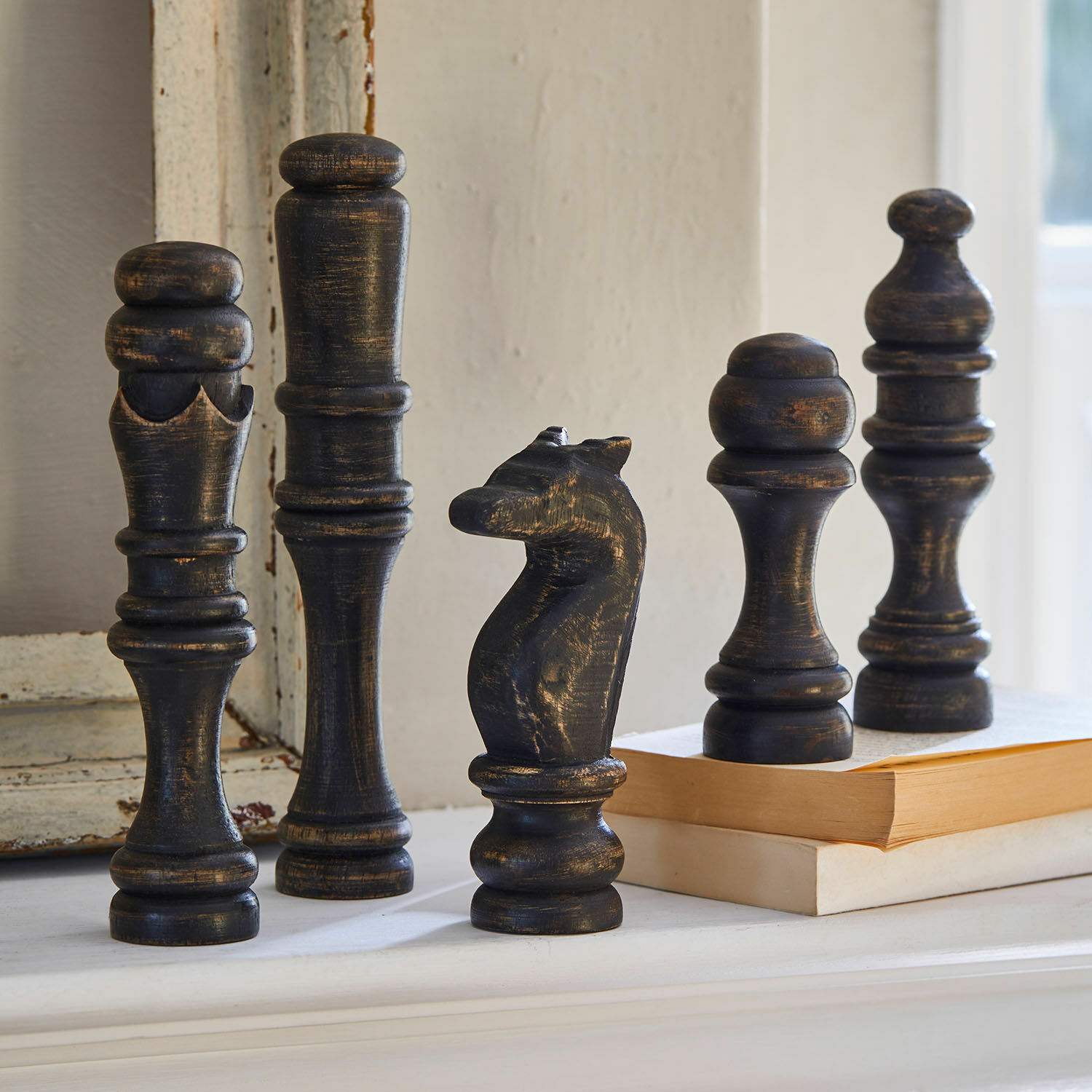 Set di 5 oggetti decorativi Guillemineau Figure da scacchi decorative in legno nero con finitura antica su una mensola accanto a libri.