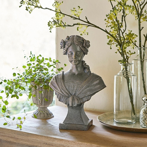 Busto femminile in pietra grigia con fiori tra i capelli su tavolo in legno con decorazioni vegetali
