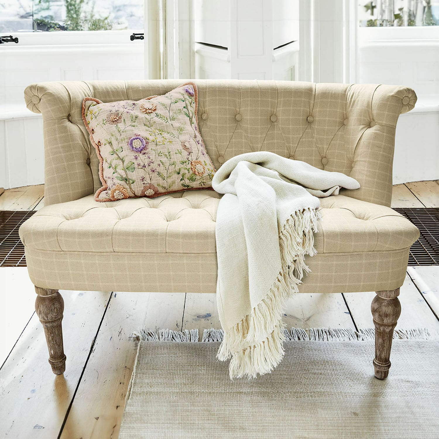 Divano Weralin Divano beige imbottito con gambe in legno, cuscino decorativo e coperta crema su tappeto chiaro