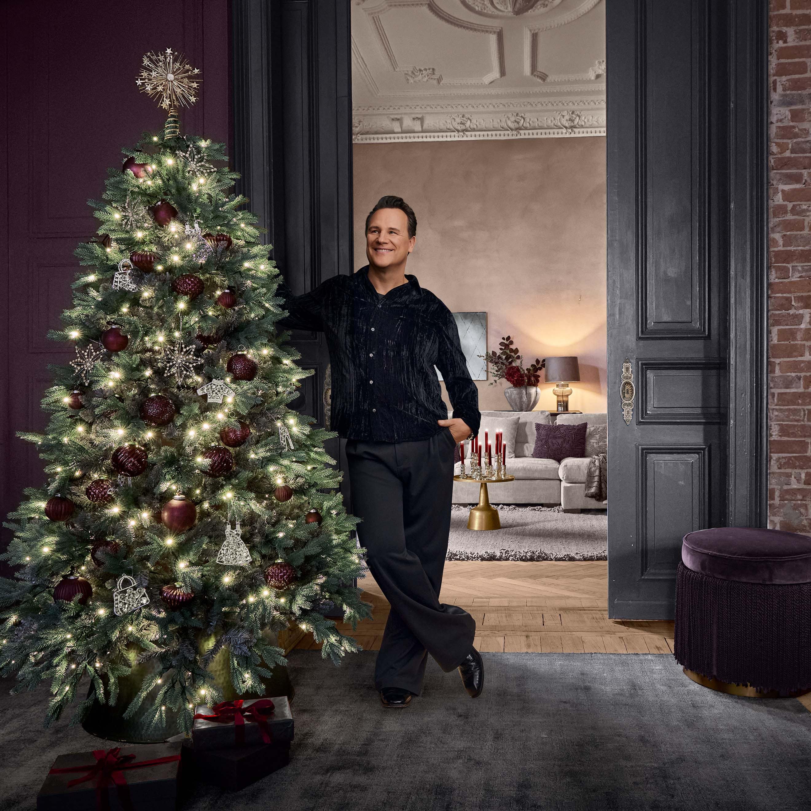 Albero di Natale decorato con palline rosse e ornamenti argento con luci in interno elegante con uomo.