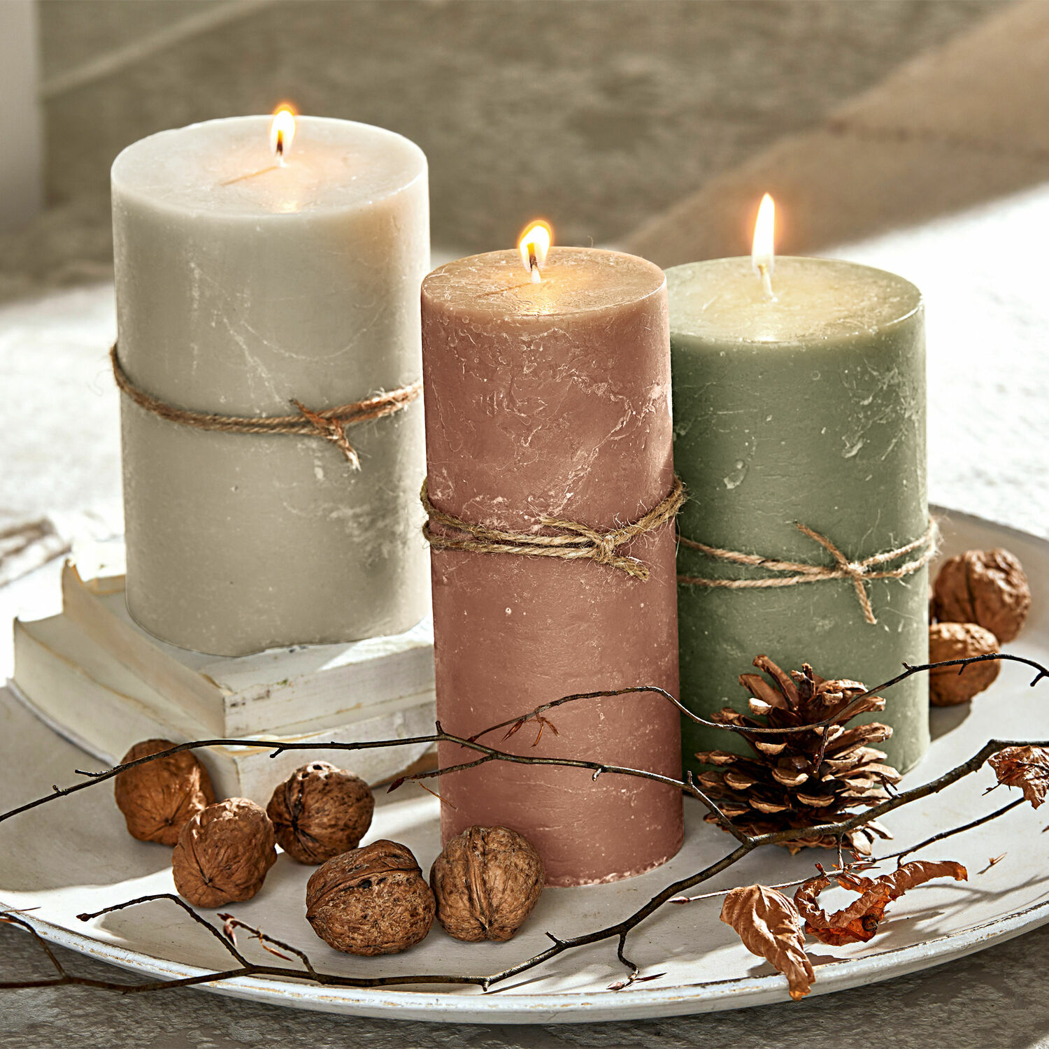 Set di 3 candele Salis Tre candele di cera accese beige, rosa e verde su un vassoio decorativo con noci e rami