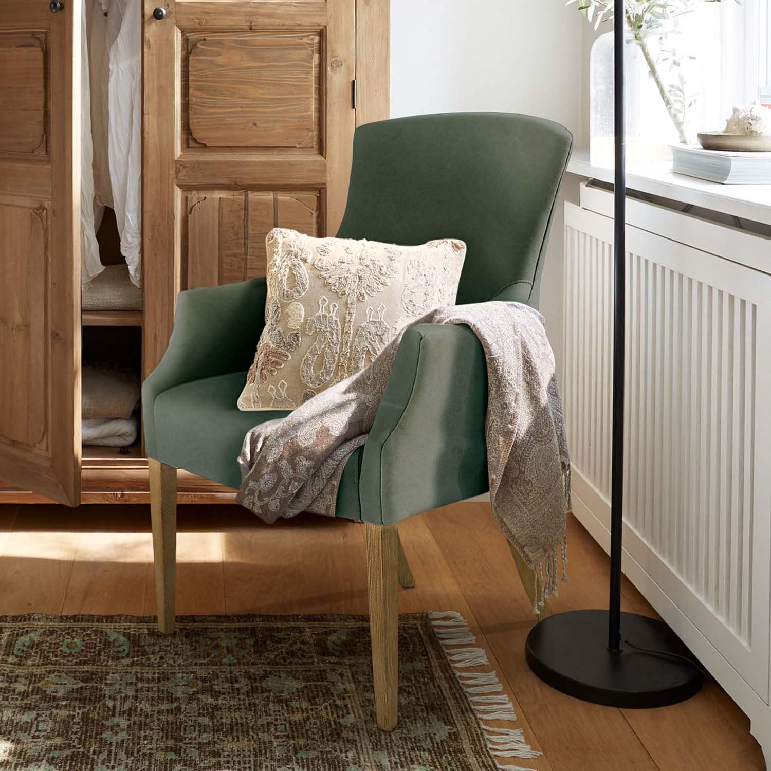 Poltrona verde rivestita con gambe in legno, cuscino decorativo e plaid grigio in ambiente accogliente