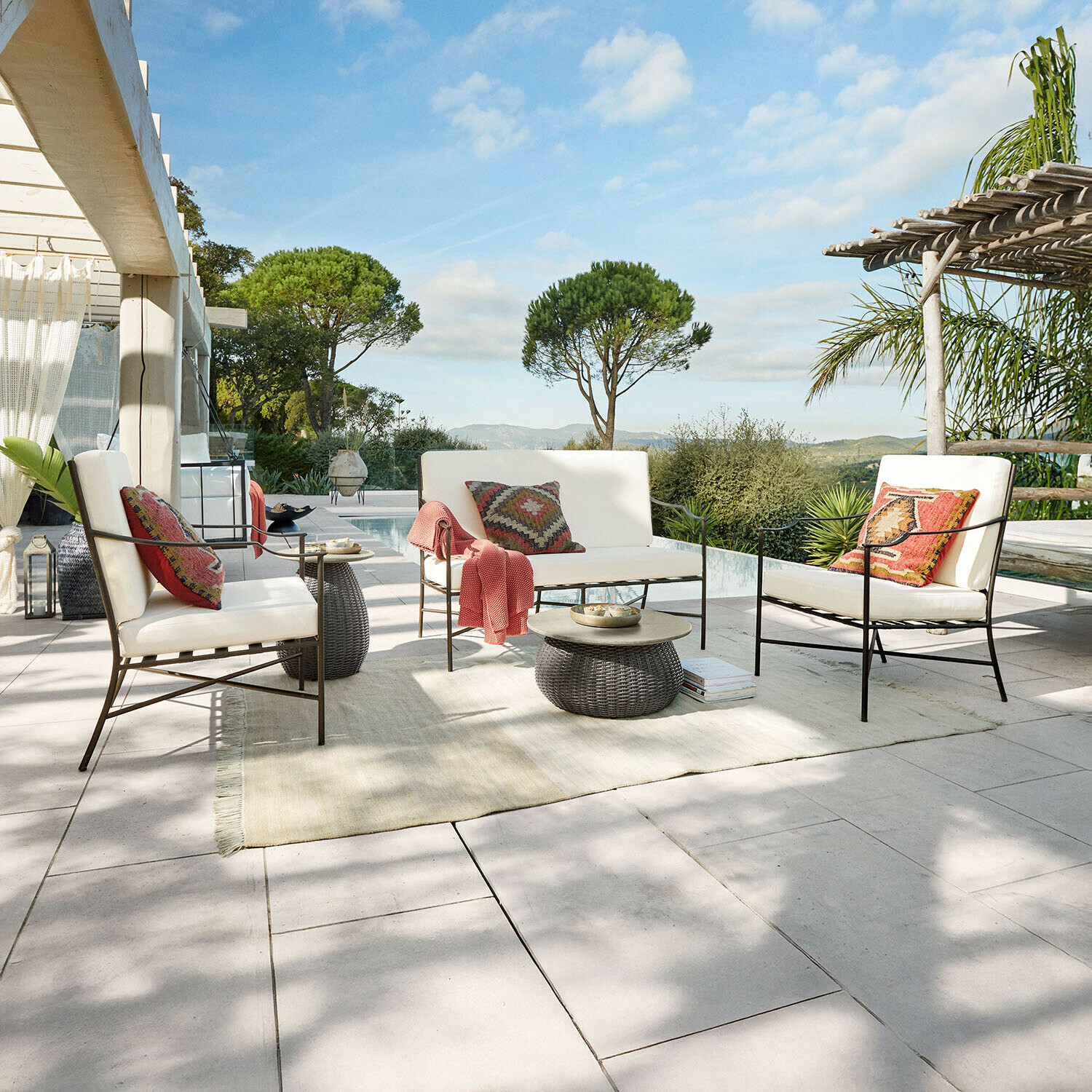 Set di mobili da giardino con struttura in metallo e cuscini crema su terrazza con vista piscina