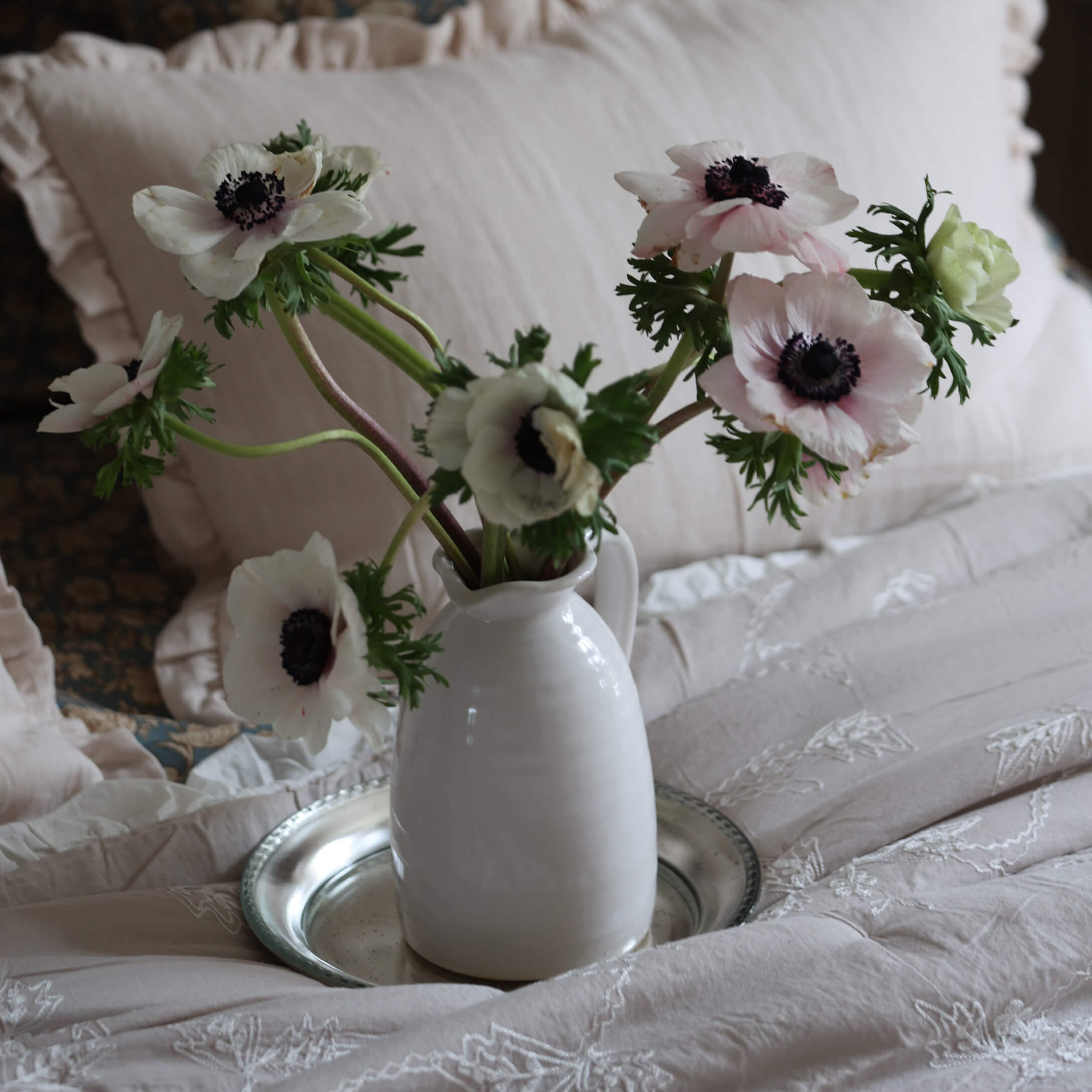 Brocca in ceramica bianca con anemoni bianchi delicati su biancheria da letto beige ricamata