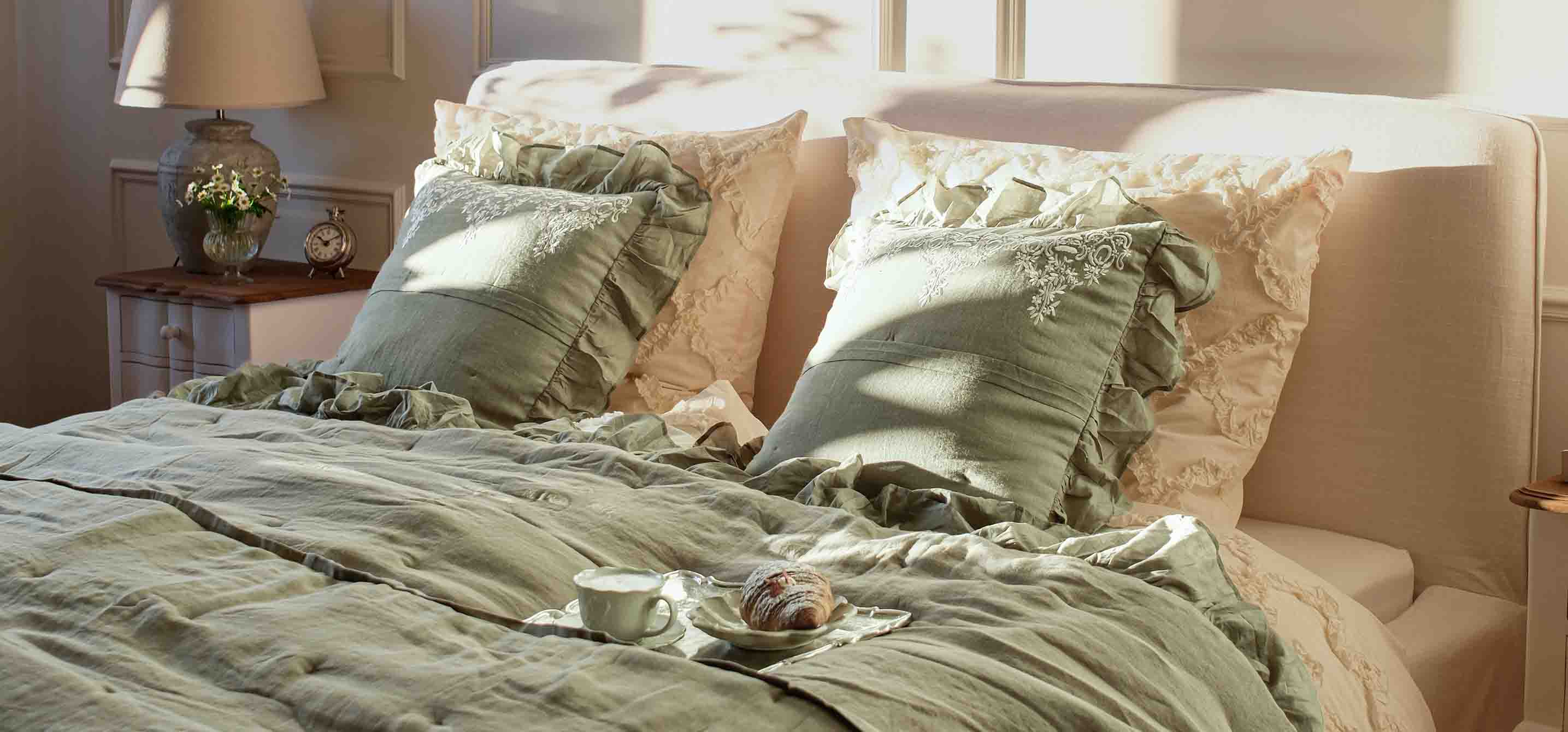 Biancheria da letto verde con cuscini arricciati su letto in camera luminosa con lampada e orologio