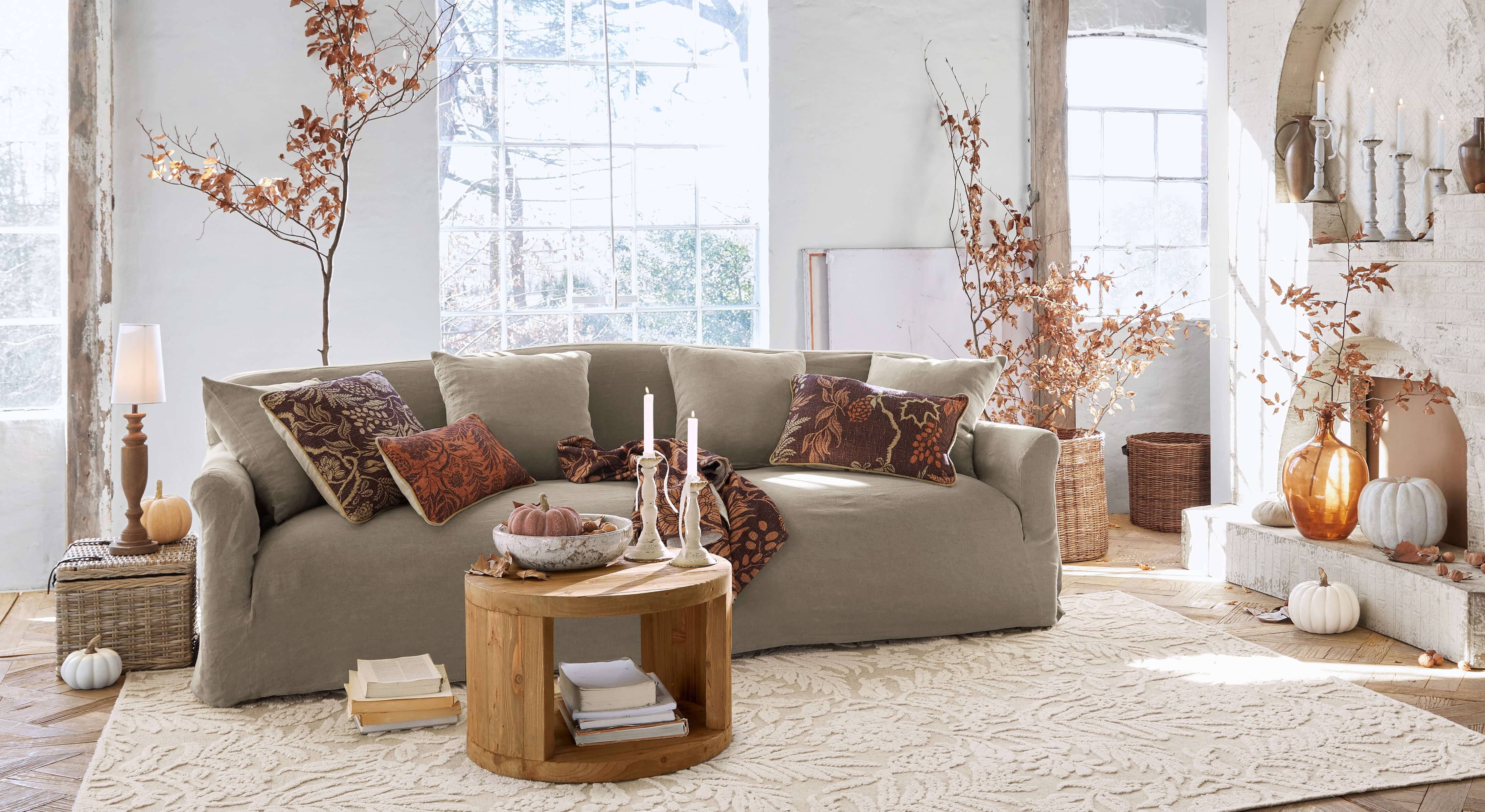 Divano beige in tessuto in soggiorno accogliente con decorazioni autunnali e tavolino in legno