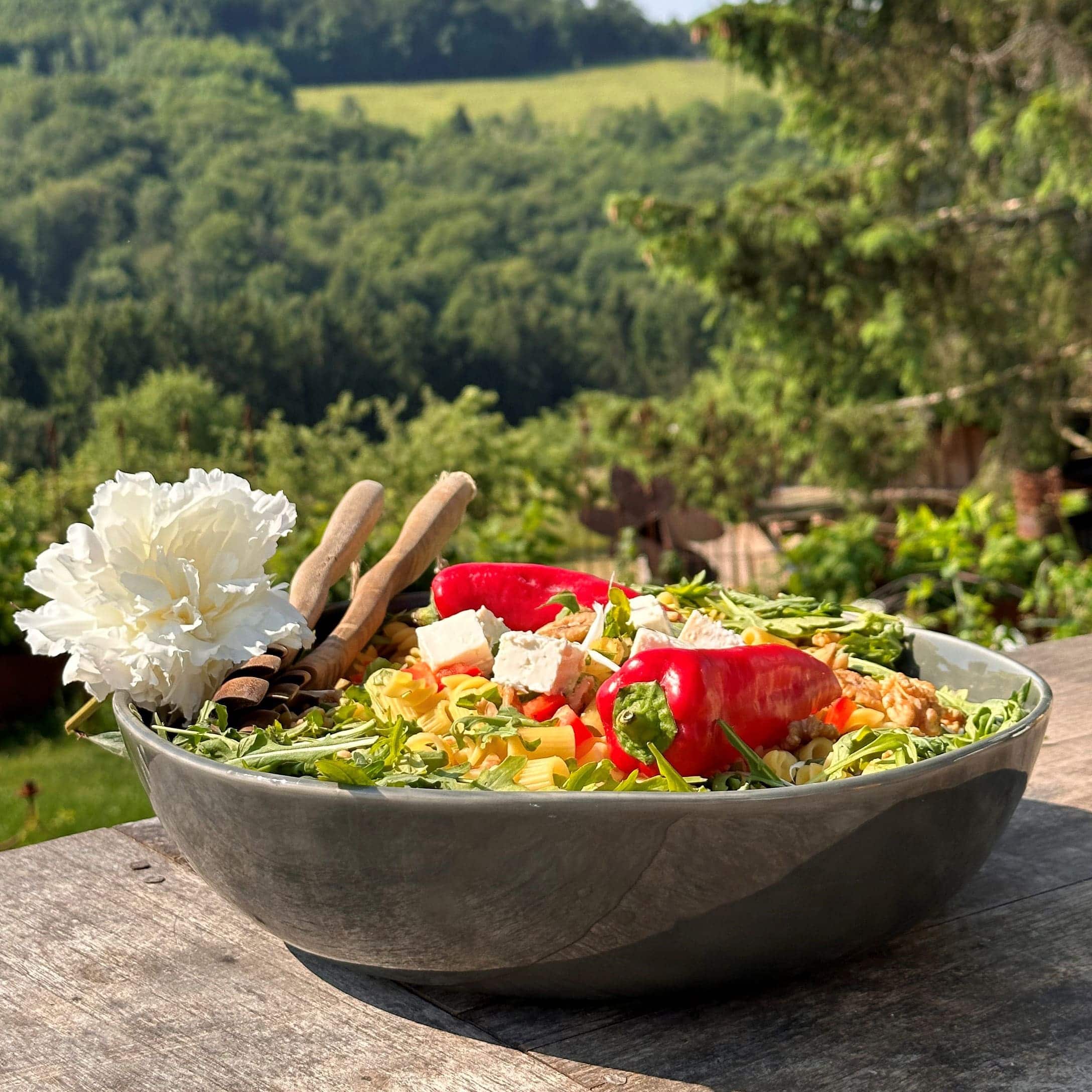 Grande ciotola in ceramica con insalata, peperoni rossi, feta e rucola su tavolo di legno all'aperto