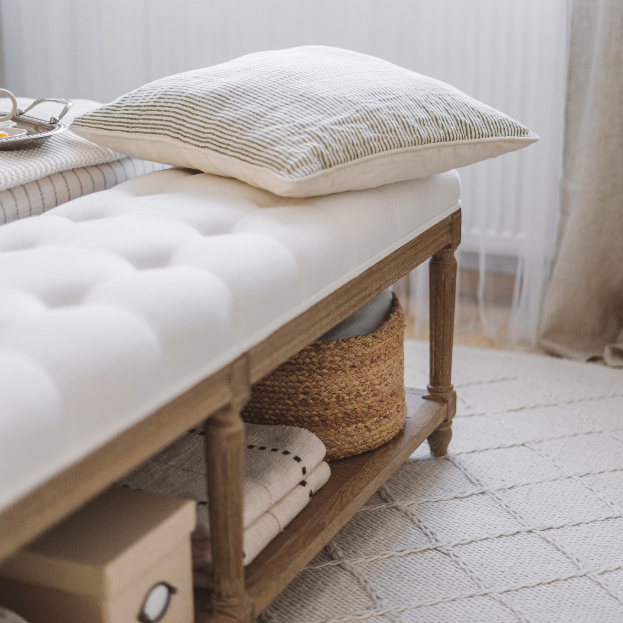 Panca in legno con seduta imbottita bianca, cuscino a righe e cesta intrecciata per riporre