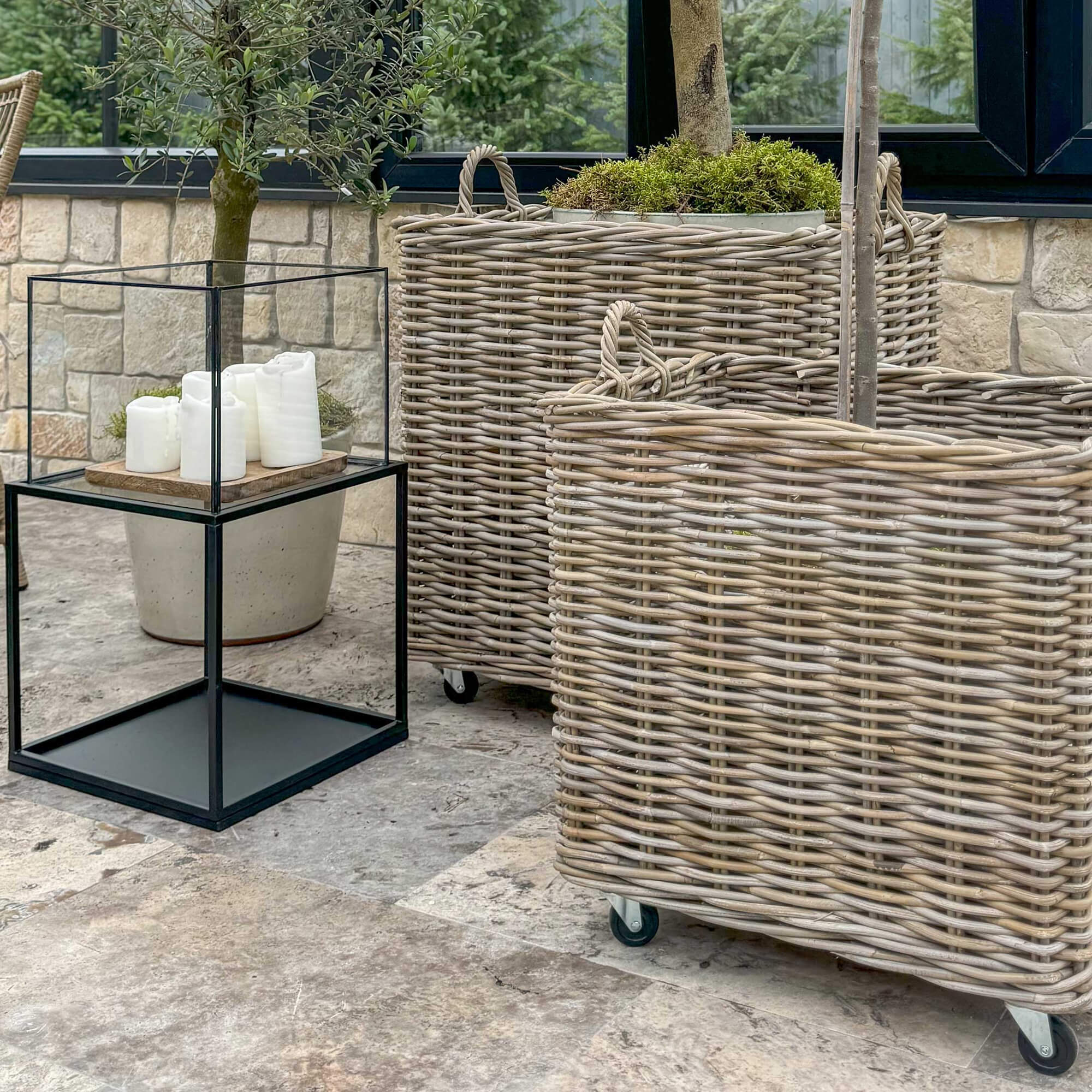 Grandi cesti in vimini naturale con ruote su terrazza con tavolino decorativo e candele bianche