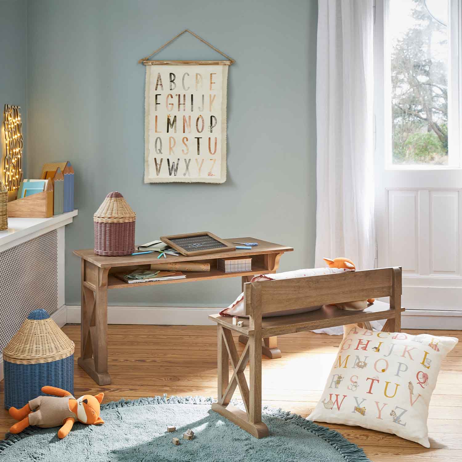 Scrivania e panca in legno in camera bambini con cuscino e decorazione alfabeto a parete