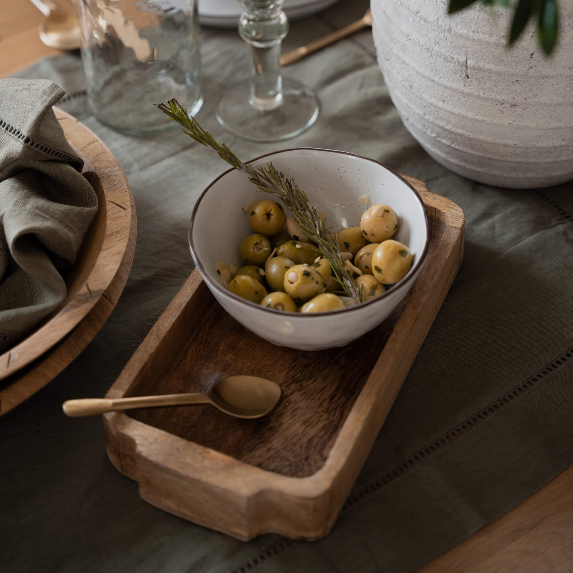 Ciotola in ceramica bianca con olive verdi e rametto di rosmarino su vassoio di legno sul tavolo