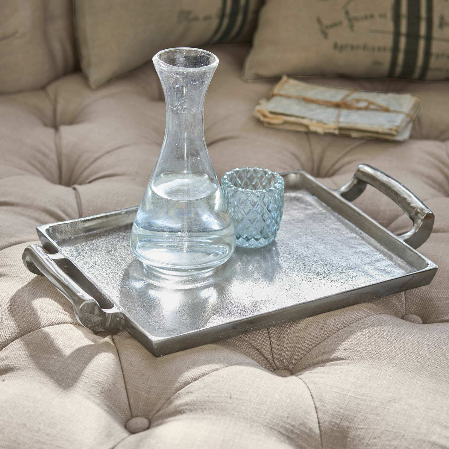 Vassoio Connaire Vassoio decorativo in metallo argentato su tessuto beige trapuntato con caraffa e bicchiere in vetro