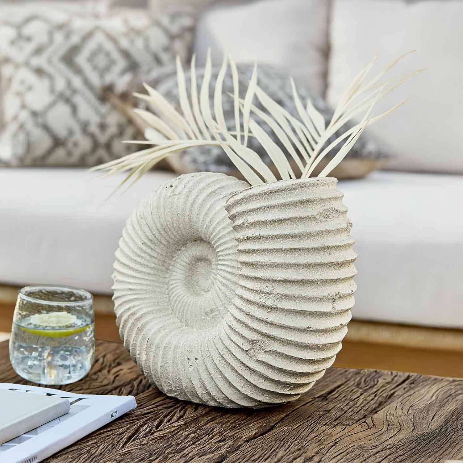 Vaso decorativo in pietra chiara a forma di conchiglia con foglie secche su tavolo in legno